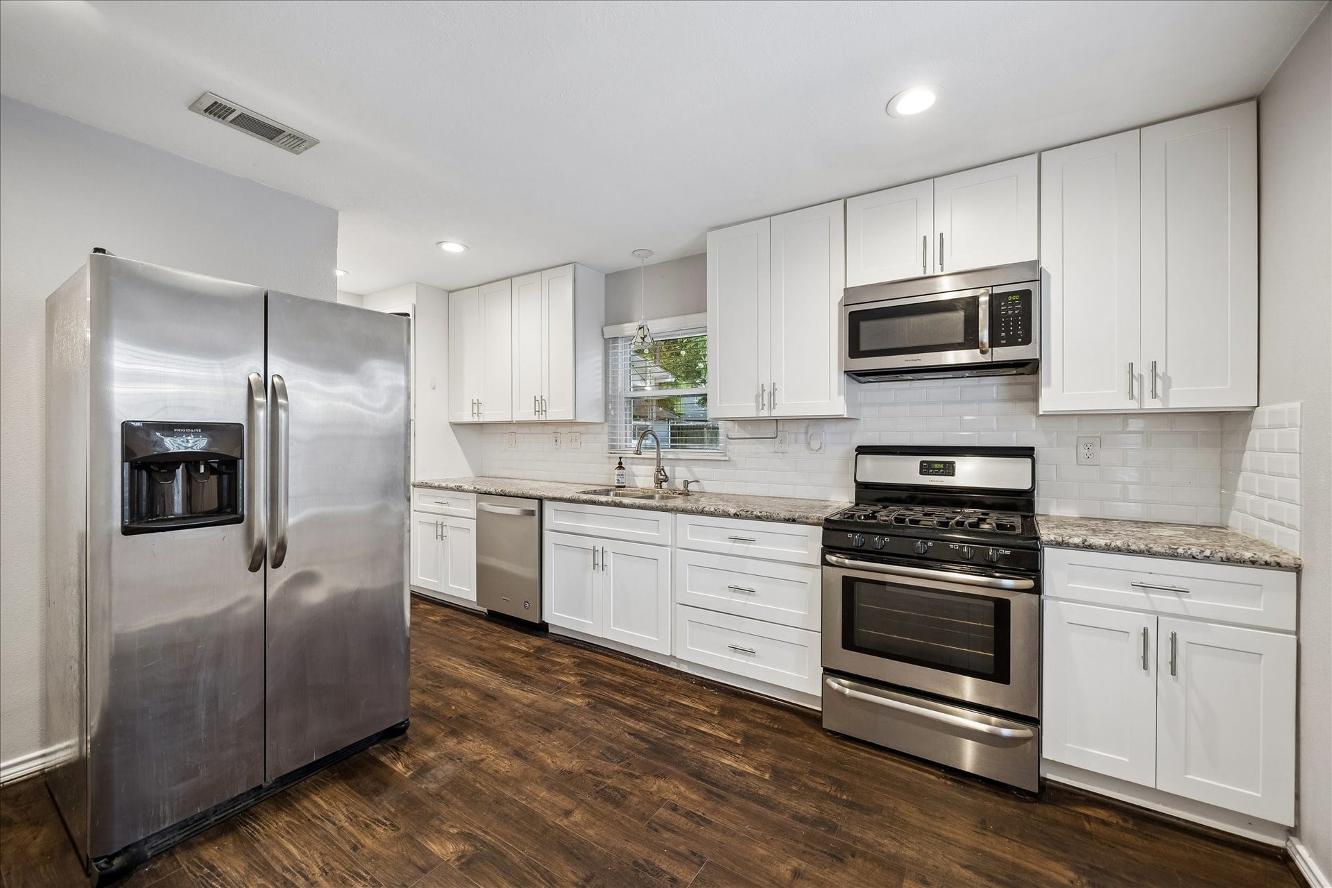 2214 Saxon Drive, Houston, TX 77018 Bright white shaker cabinetry extends to the ceiling, offering abundant storage alongside granite countertops, a subway tile backsplash, and stainless steel appliances. A thoughtful layout provides generous prep space while keeping the kitchen open to the adjoining breakfast nook and living areas.