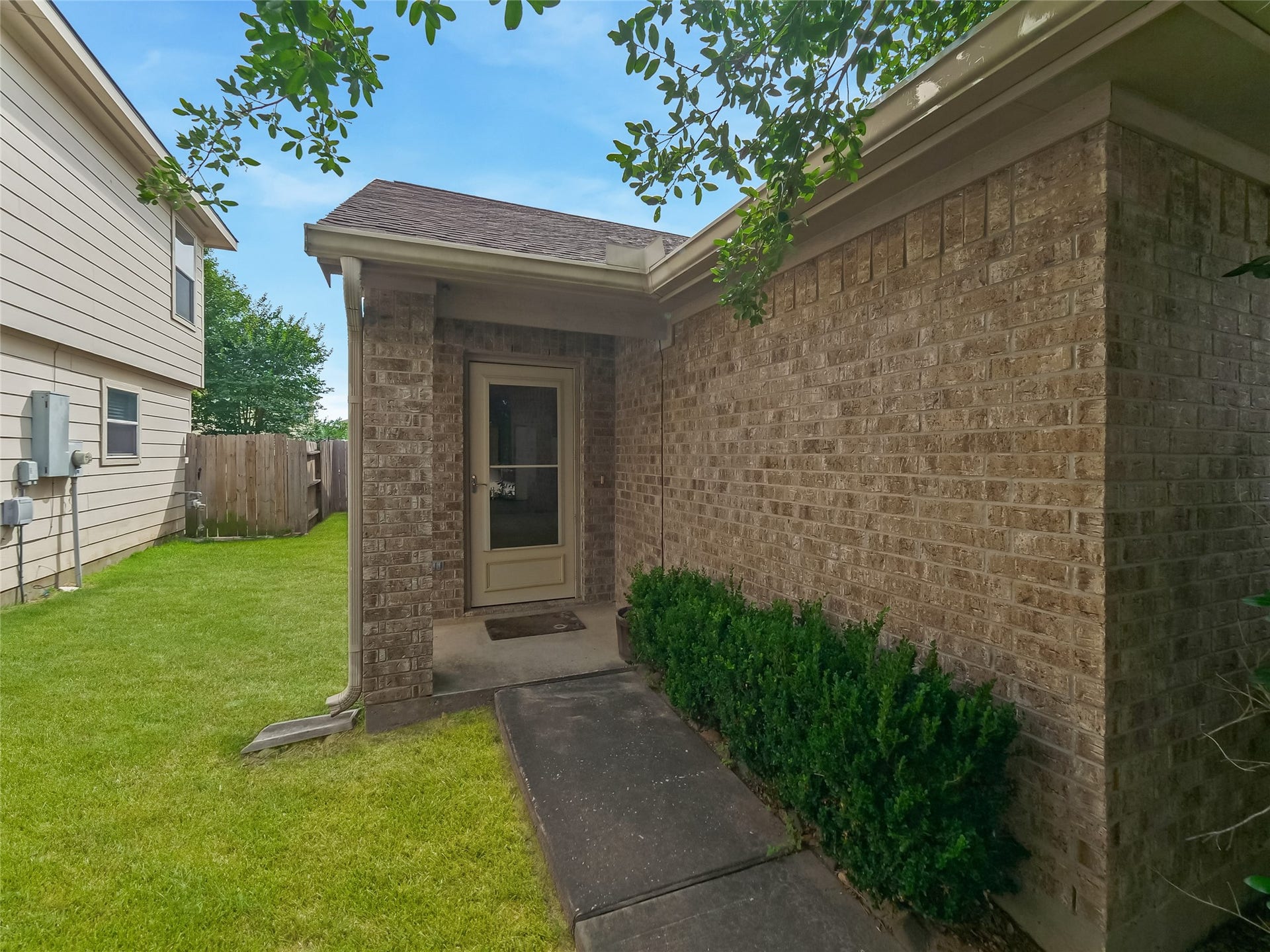 20911 Harvest Terrace Lane, Spring, TX 77379 Side entrance of the home with a brick exterior, front door, and neatly trimmed shrubs.