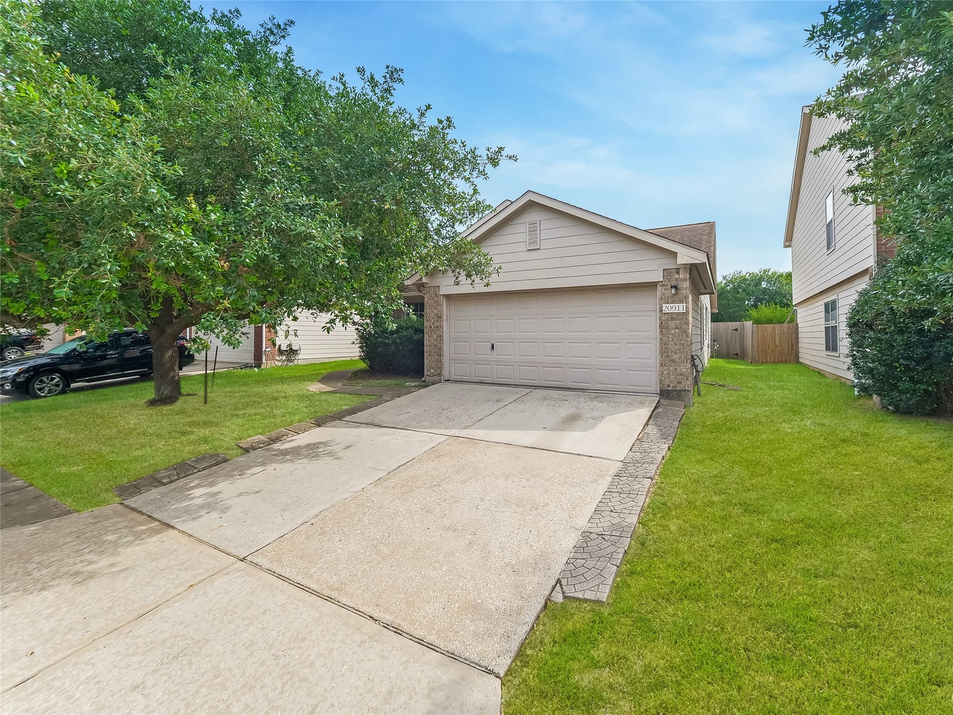 20911 Harvest Terrace Lane, Spring, TX 77379 Wide view of the house and driveway, showing the attached garage, front lawn, and surrounding trees.