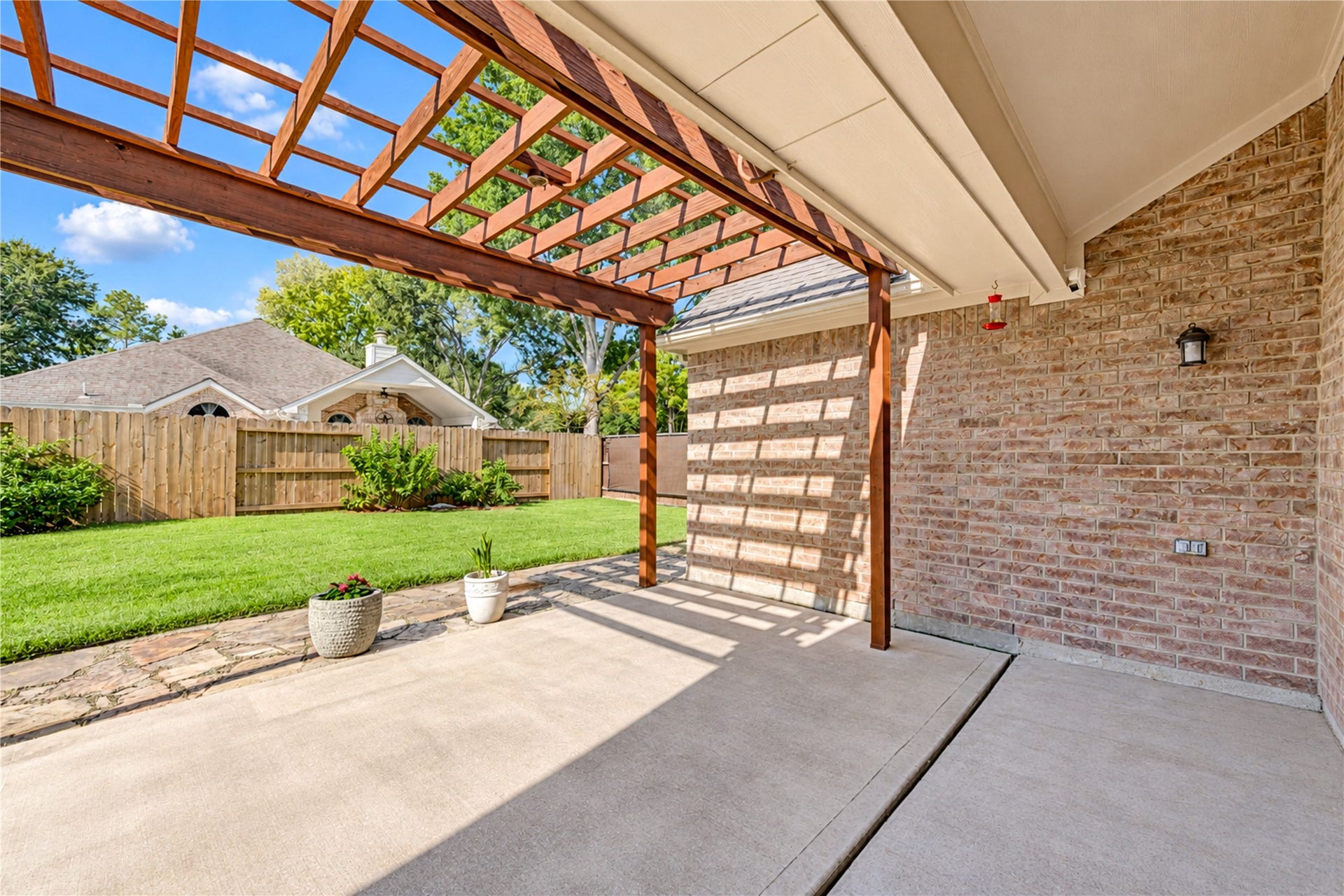 Enjoy outdoor living on the covered back patio featuring a beautiful wood pergola, ample space for seating, and a private backyard with a combination of lawn and stone accents.