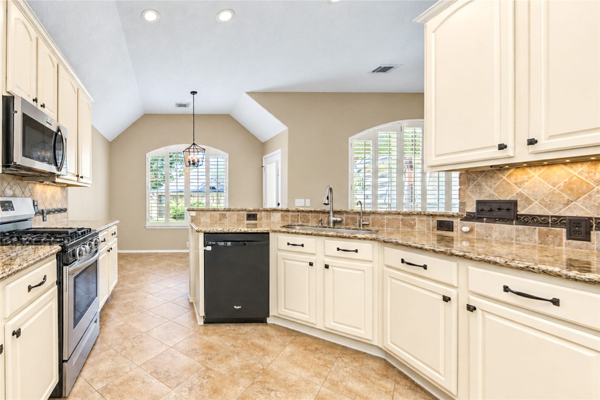 Bright kitchen featuring abundant white cabinetry, granite countertops, decorative tile backsplash, stainless steel appliances, a gas range, and a breakfast bar overlooking the dining area.