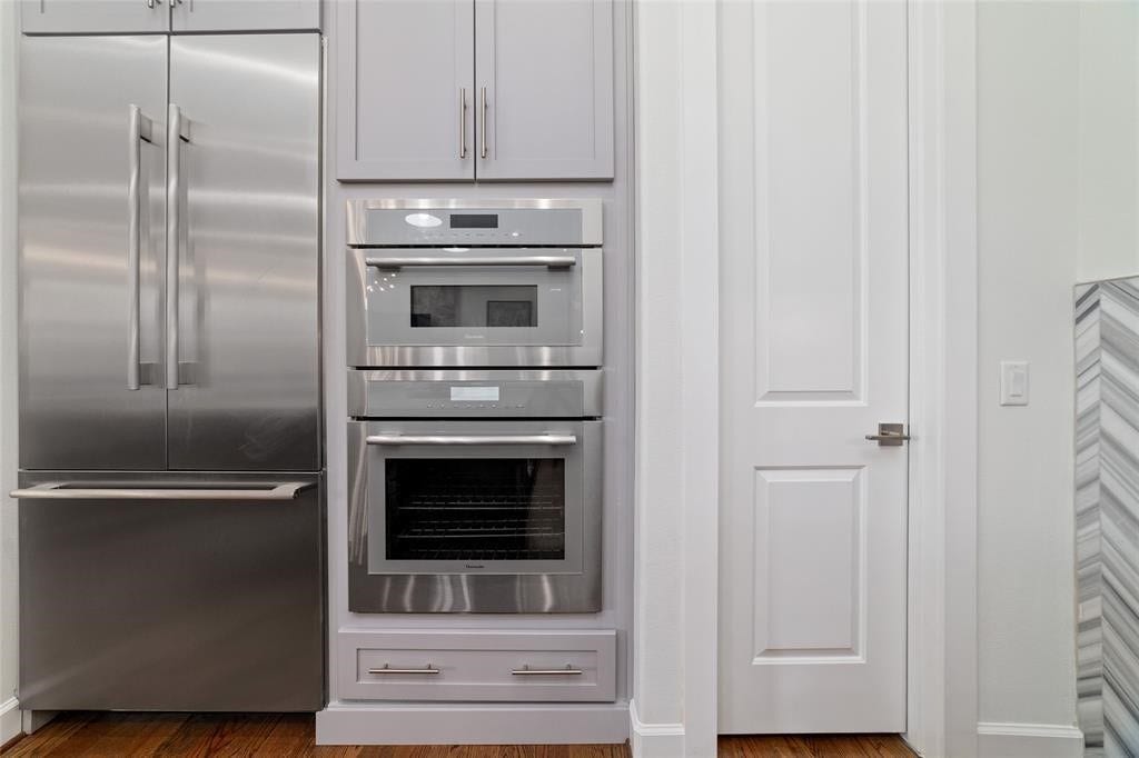 This kitchen features modern stainless steel appliances, including a double-door refrigerator and built-in ovens. The cabinetry is sleek and complements the contemporary design, while the hardwood floors add warmth to the space.
