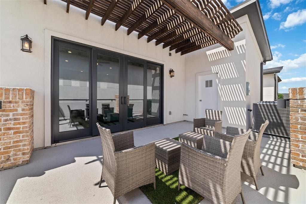 This inviting outdoor patio features a modern pergola, and large glass doors leading inside. It's perfect for relaxing and entertaining, with a stylish blend of brick and stucco elements.