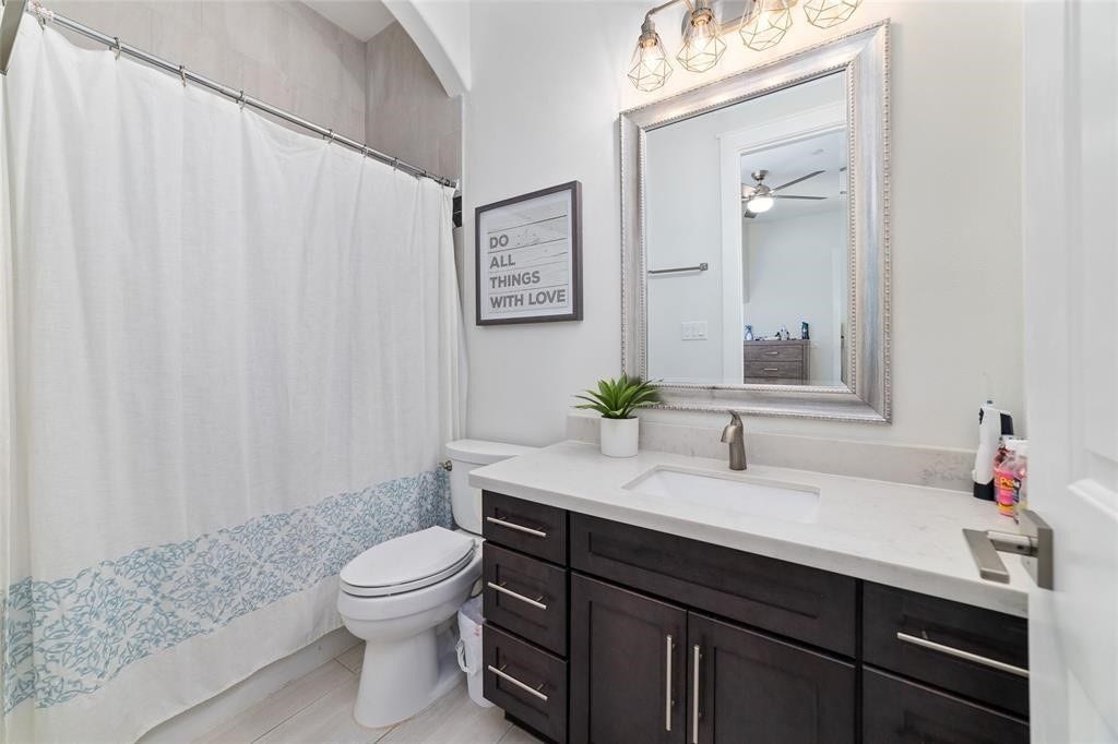 This bathroom features a modern design with a dark wood vanity, a white countertop, and a sleek sink. It includes a large framed mirror with stylish lighting above and light flooring.