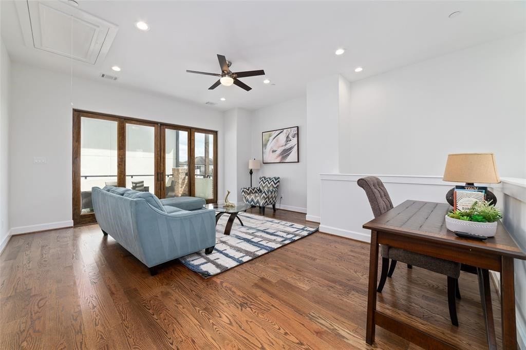 This photo showcases a bright, open living space with hardwood floors, modern ceiling fan, and ample natural light from large glass doors.