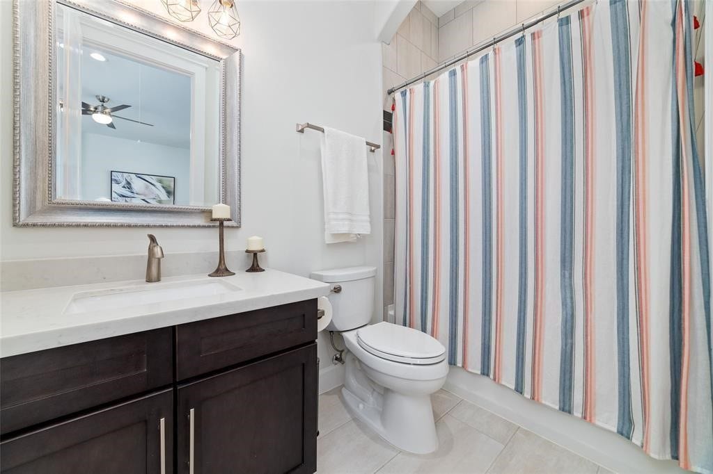 The bathroom features a modern vanity with a sleek countertop and stylish fixtures. It has a large framed mirror, a toilet, and a bathtub. The space is well-lit and has a clean, contemporary design.
