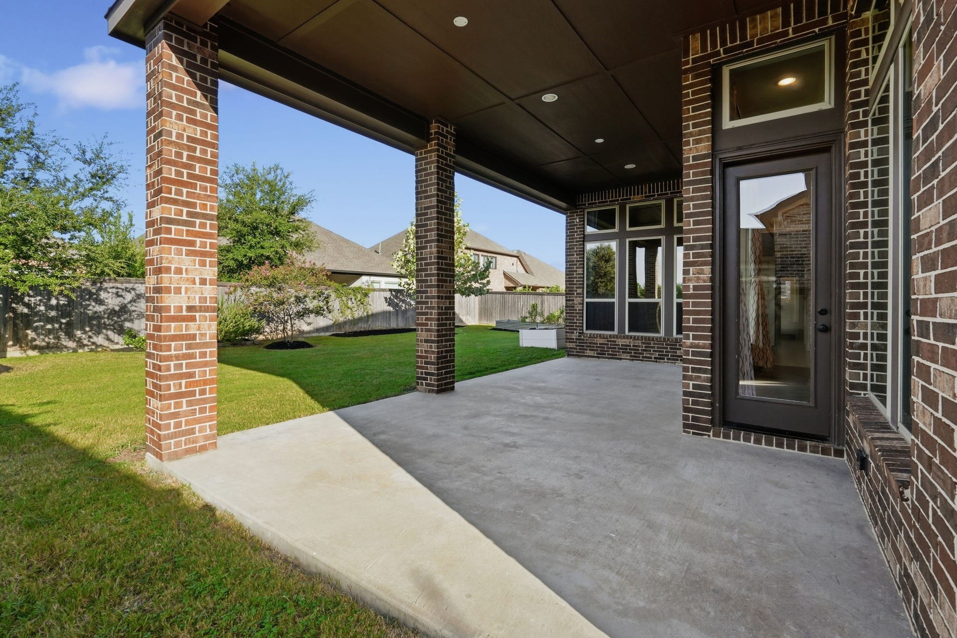 15223 Prairie Dog Town Lane, Cypress, TX 77433 Covered patio offering a generous outdoor living space with a spacious concrete area, brick columns, and views of the beautifully landscaped backyard.