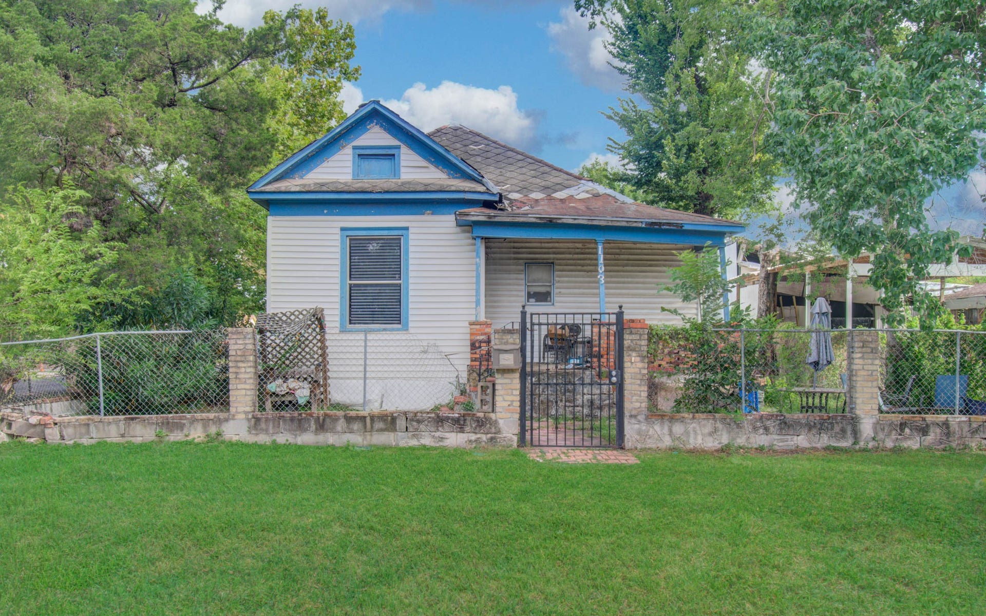 1103 Harrington Street, Houston, TX 77009 Fixer-upper with potential, featuring a quaint front porch, fenced yard, and mature trees.