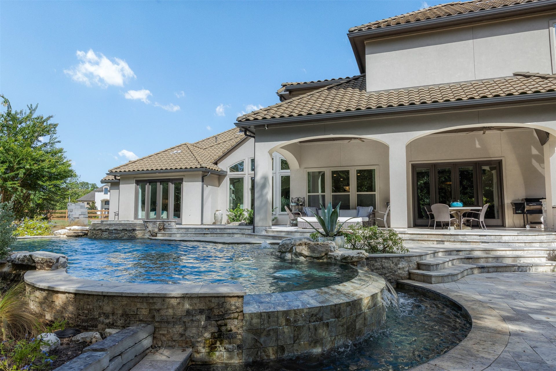 8603 Woods Hollow Trail, Fulshear, TX 77406 Infinity edge pool with colored lights surrounded by travertine decking.