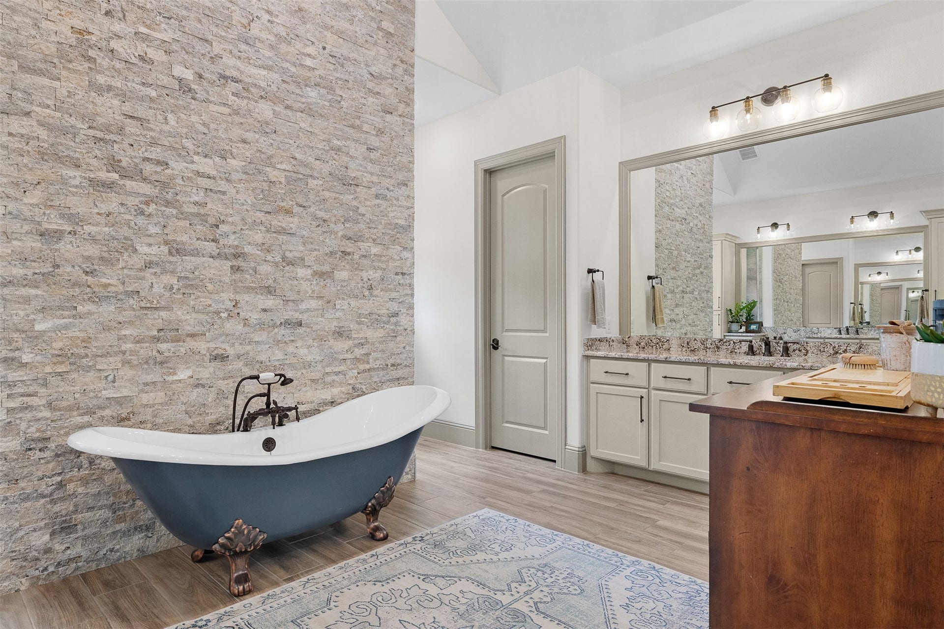 8603 Woods Hollow Trail, Fulshear, TX 77406 Rock accent wall in the primary bath anchors the custom teal colored, clawfoot soaking tub.