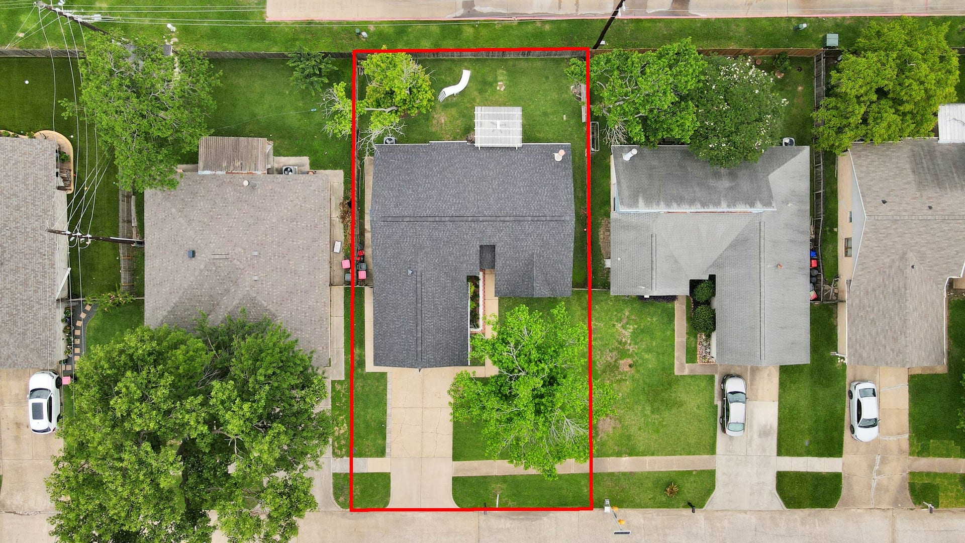 This aerial view highlights a well-maintained property with a spacious backyard, outlined in red. The home features a driveway and is situated in a neighborhood with similar houses, offering ample green space and a quiet setting.