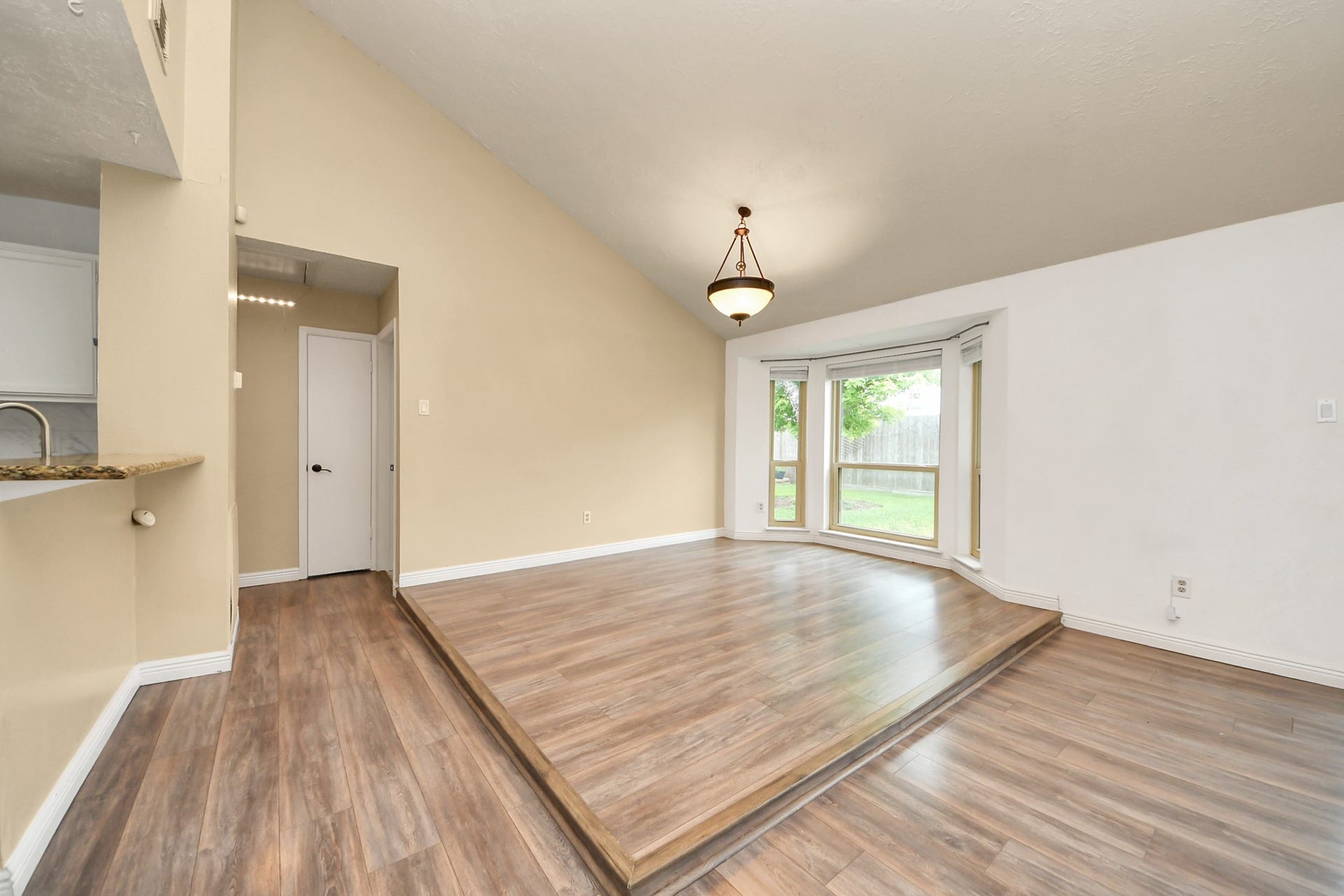 This room features a raised platform with large bay windows offering plenty of natural light. The space has high ceilings, wood flooring, and a modern light fixture, creating a bright and open atmosphere.