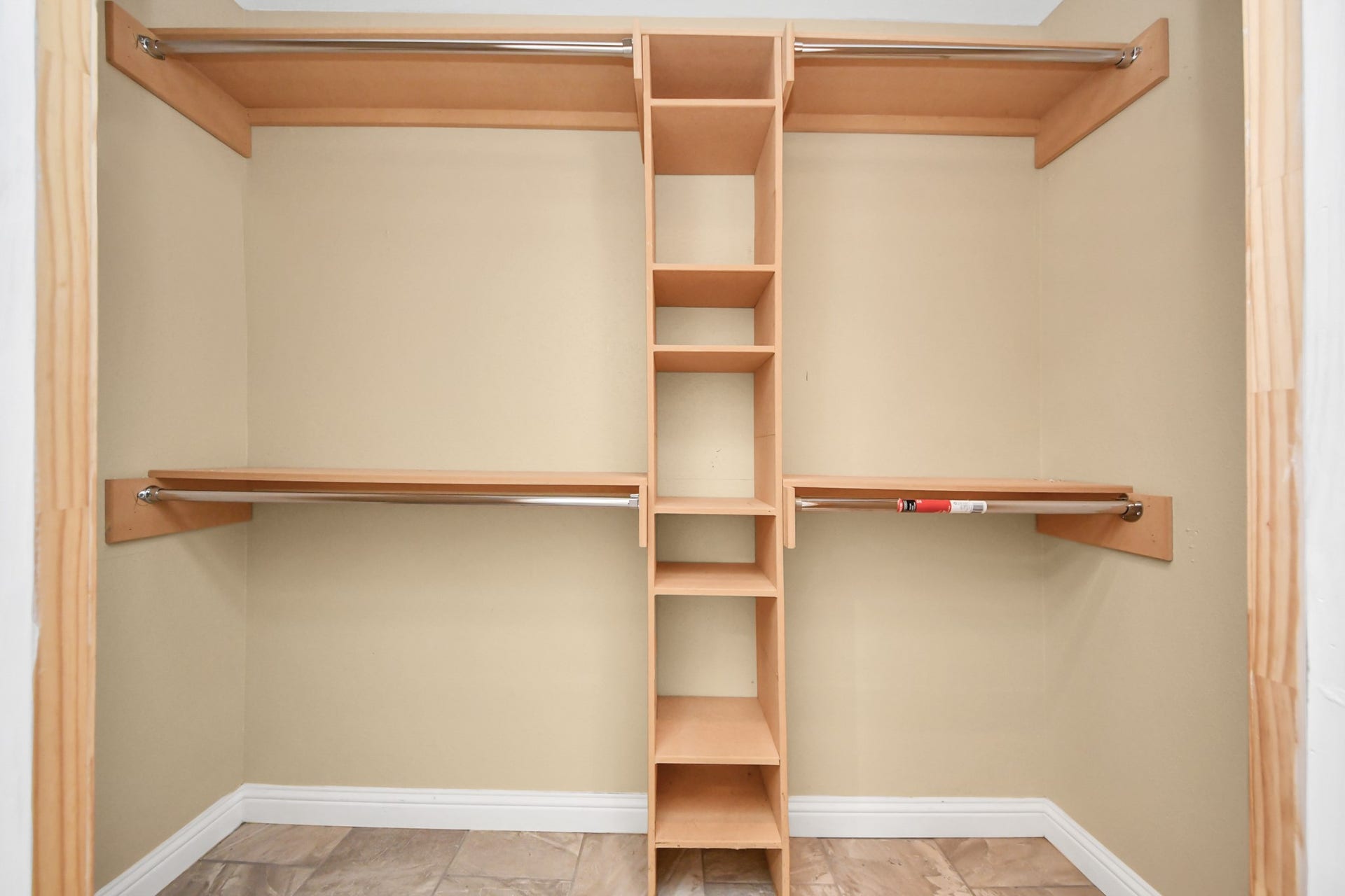 This is a spacious walk-in closet with a neutral color scheme, featuring multiple hanging rods and center shelving for organized storage. The tiled flooring adds a touch of elegance.