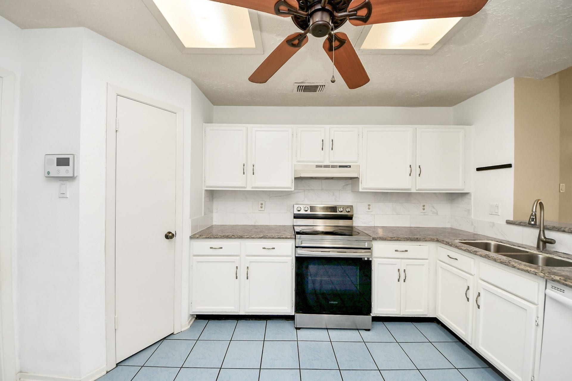 This kitchen features modern stainless steel appliances, white cabinetry, and granite countertops. The kitchen offers a breakfast area with a ceiling fan. The layout includes a double sink and a convenient corner design for efficient use of space.