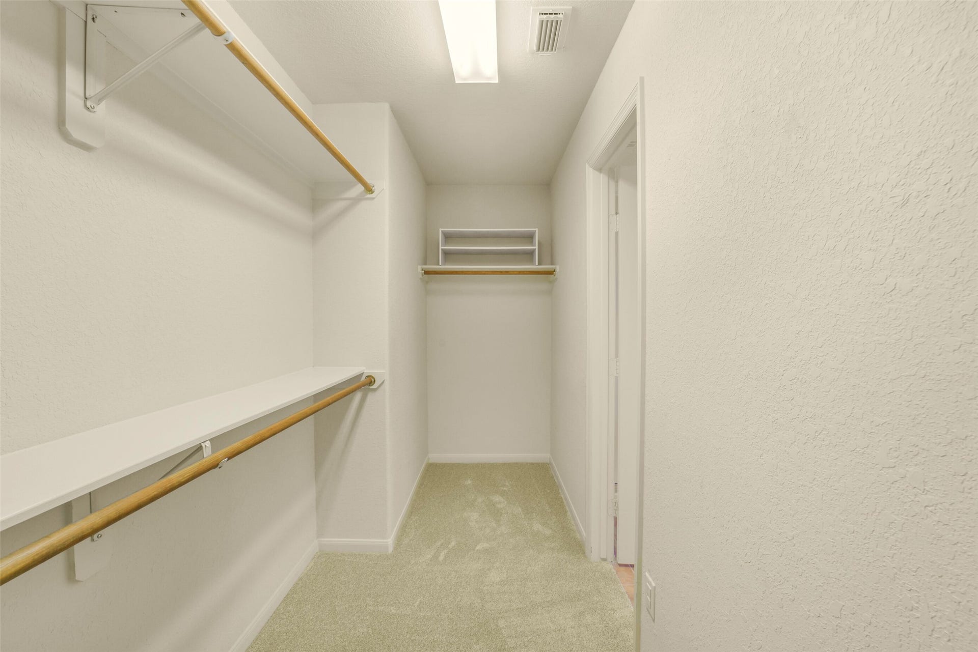 Spacious primary walk-in closet with ample shelving and hanging space, featuring soft carpeting and a bright overhead light.