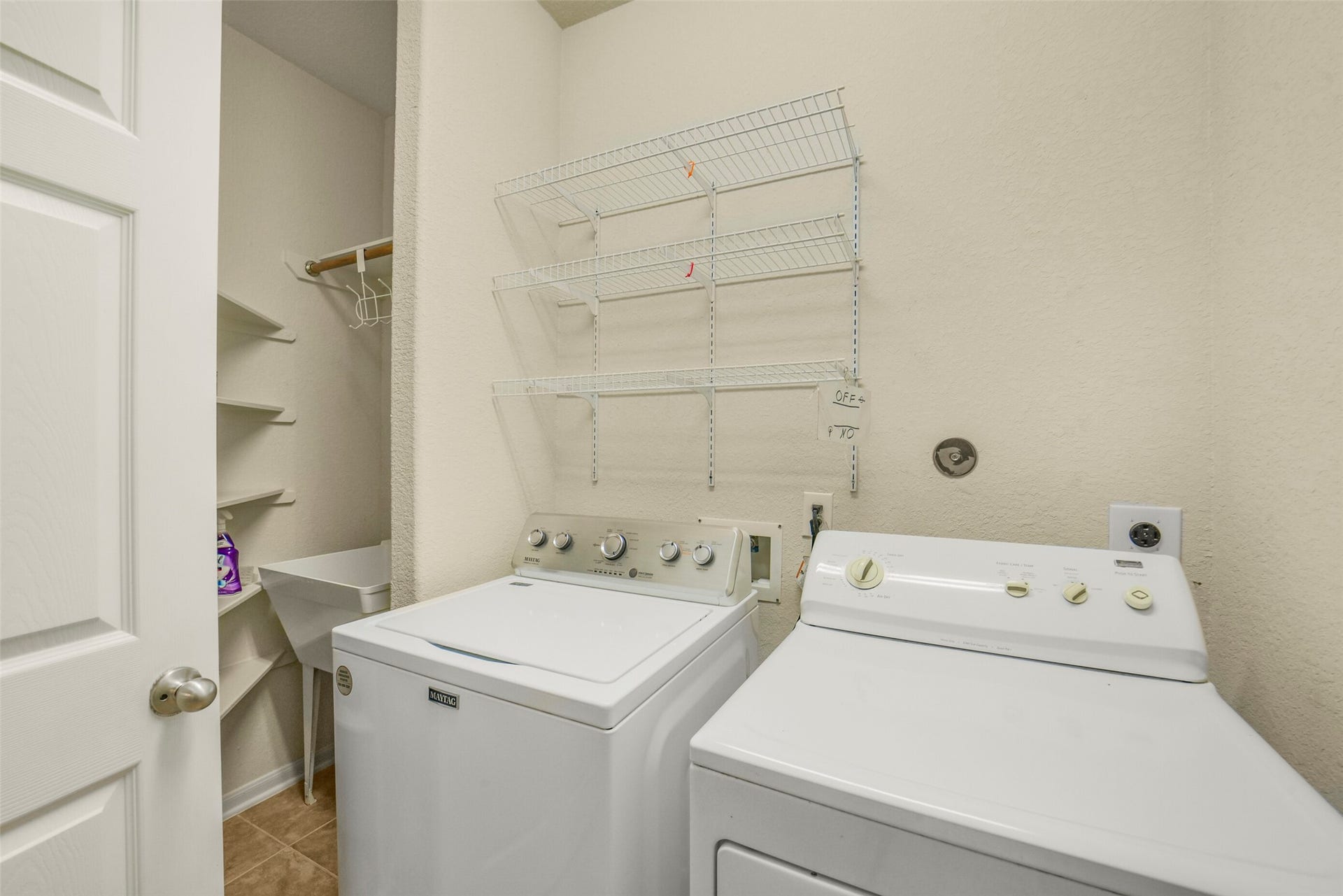 Large laundry room with washer and dryer, ample shelving, and a utility sink for added functionality.