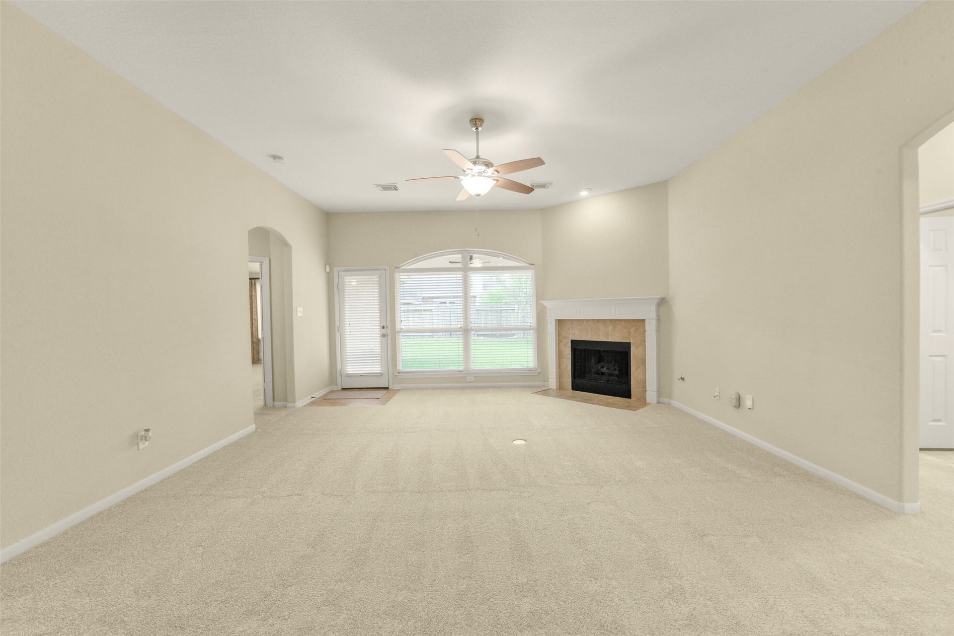 Spacious living room with plush carpeting, a cozy fireplace, large windows for natural light, and a ceiling fan, offering comfort and style.