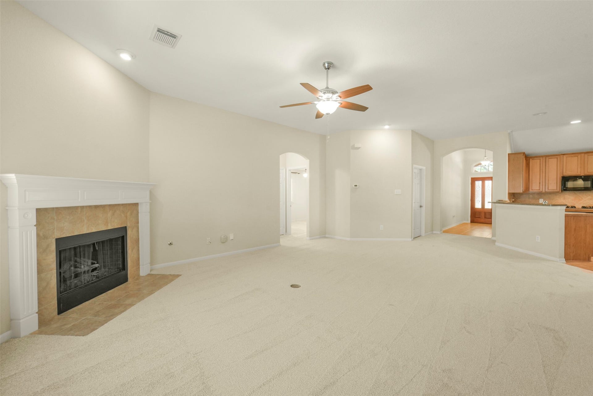 Spacious living room with plush carpeting, a cozy fireplace, and an open layout leading to a modern kitchen with wood cabinetry.