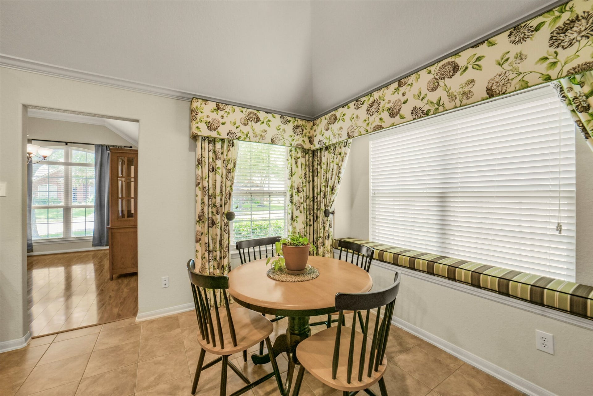 Charming breakfast nook with a cozy table set, surrounded by large windows adorned with floral curtains, offering a bright and inviting space.