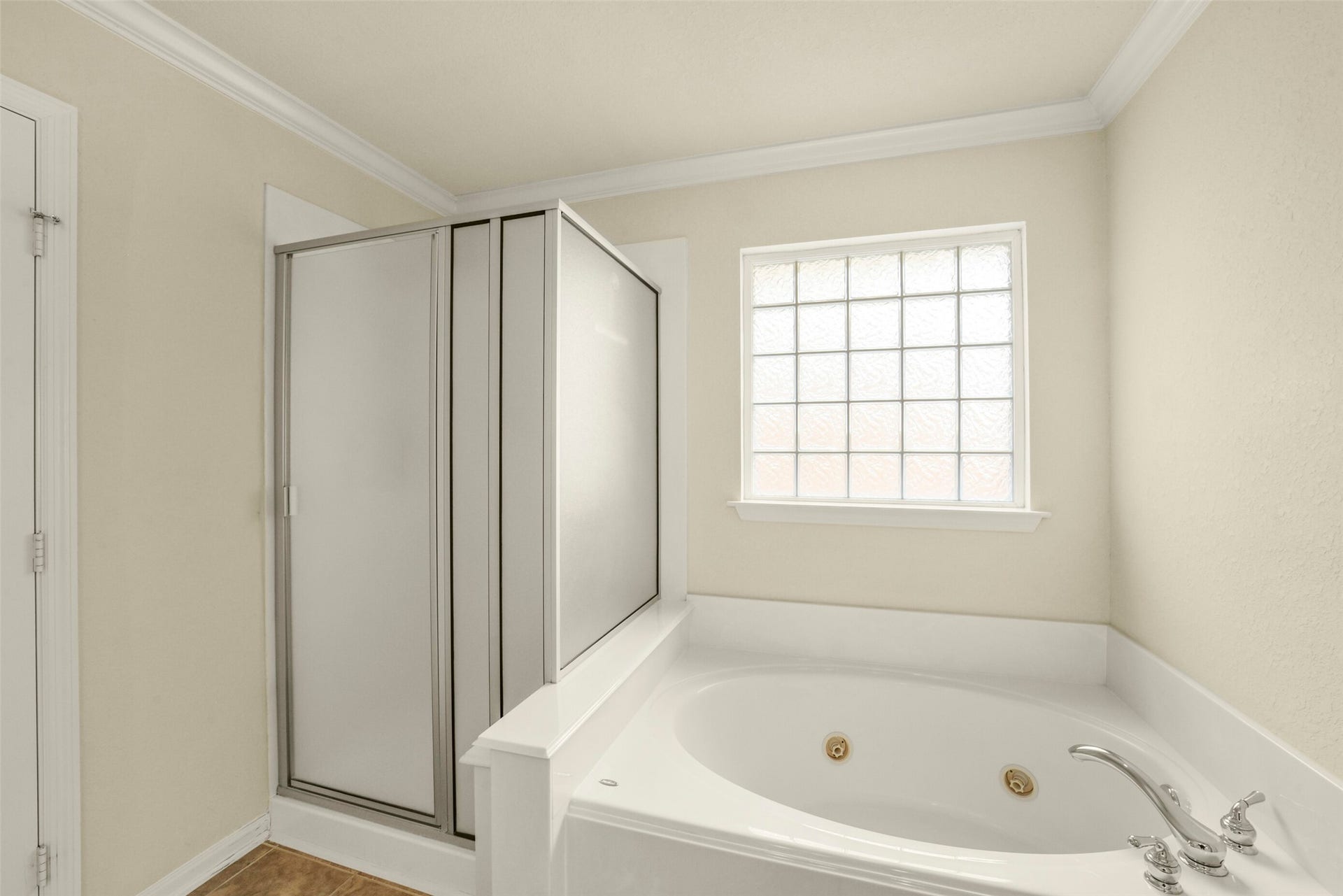 The primary bathroom featuring a luxurious corner jetted tub and separate shower, illuminated by a frosted window for natural light and privacy.