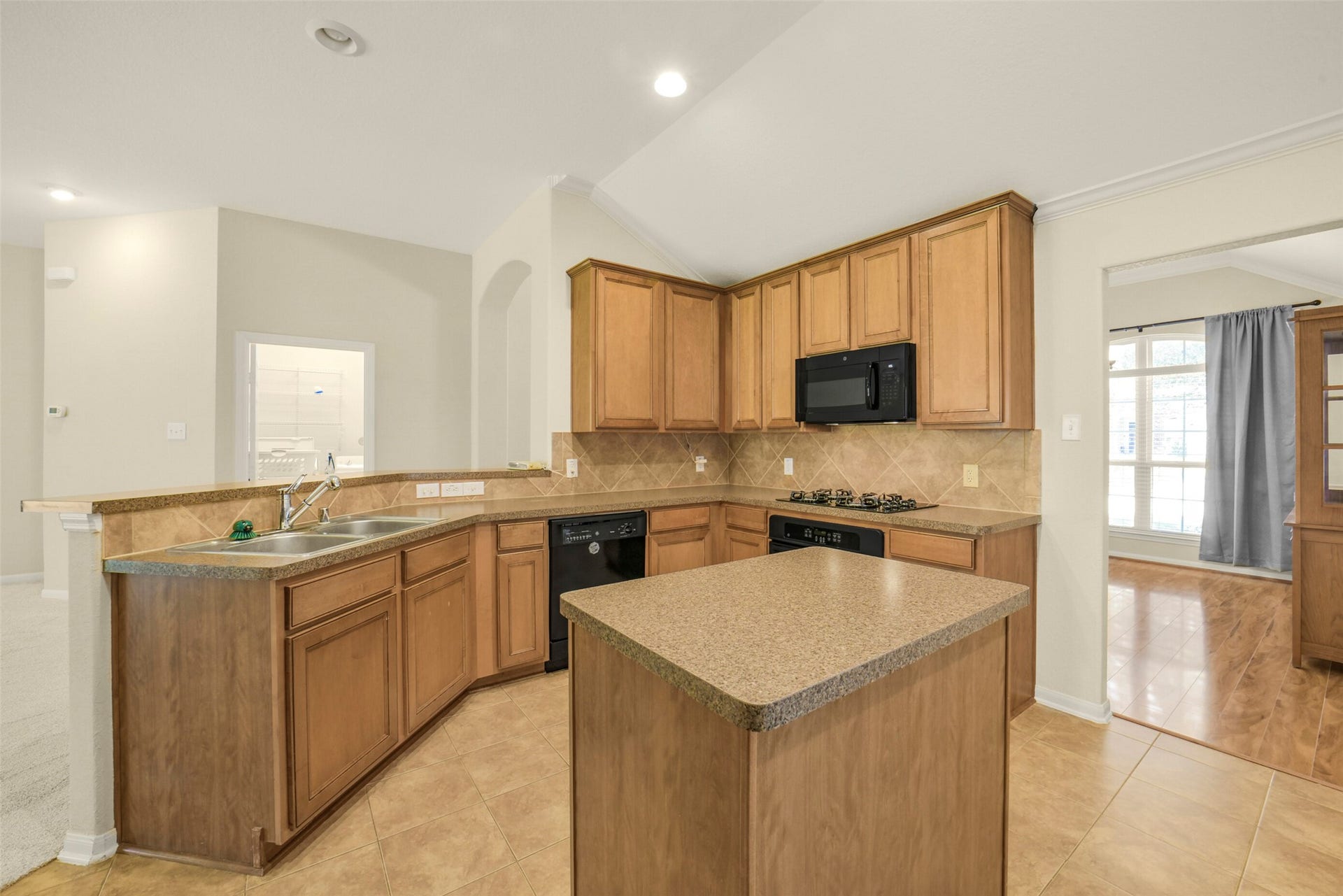 Spacious kitchen with warm wood cabinetry, a central island, and modern appliances, perfect for culinary enthusiasts.