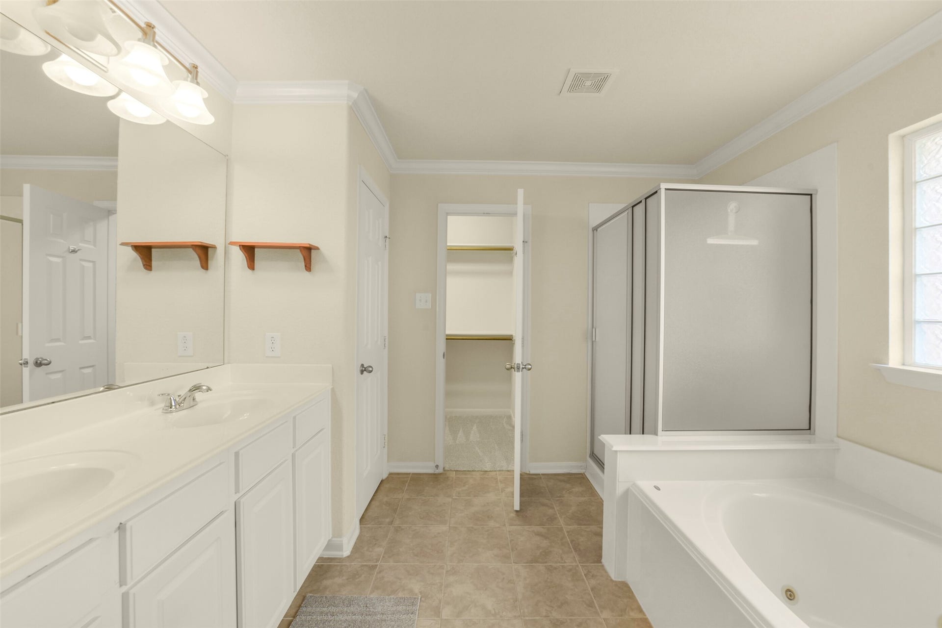 Spacious primary bathroom featuring a dual-sink vanity, large soaking tub, separate shower, and convenient walk-in closet.