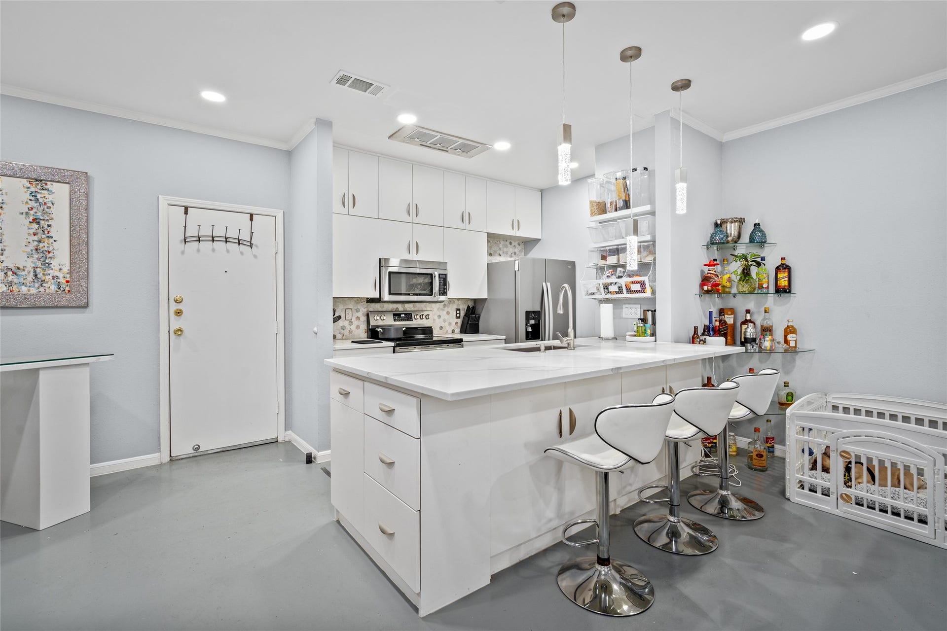 9850 Pagewood Lane, #1302, Houston, TX 77042 This stylish and functional kitchen features sleek white cabinetry, stainless steel appliances, and a stunning quartz countertop island with a breakfast bar. Pendant lighting adds a contemporary touch, while open shelving provides convenient storage. The adjacent bar area offers additional space for entertaining, making this kitchen perfect for hosting and everyday living.