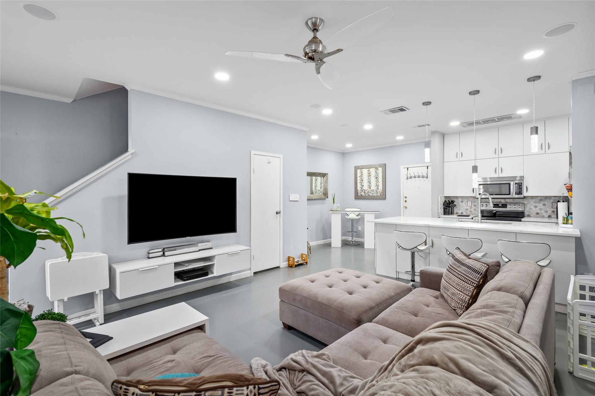 9850 Pagewood Lane, #1302, Houston, TX 77042 This beautifully designed open-concept living space seamlessly connects to the modern kitchen, creating an ideal layout for both relaxation and entertaining. The spacious living area features recessed lighting, a sleek ceiling fan, and a neutral color palette that enhances the home's contemporary feel. The kitchen boasts crisp white cabinetry, stylish pendant lighting, and a large island with bar seatingperfect for casual dining or gathering with guests.
