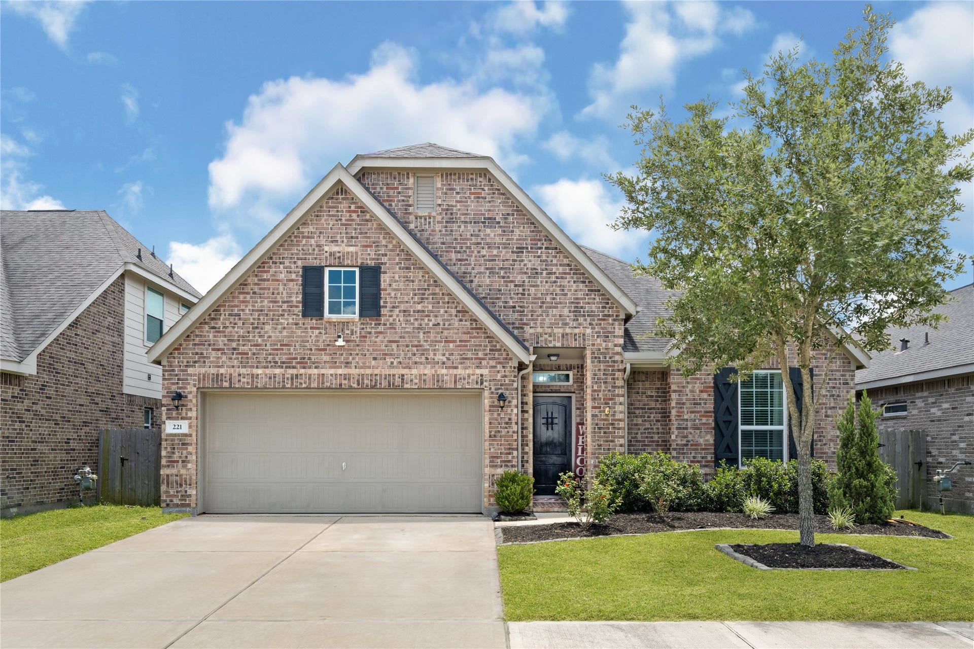 This charming home features a classic brick exterior with a spacious two-car garage. The well-maintained front yard includes a manicured lawn, small shrubs, and a tree, adding to its curb appeal.