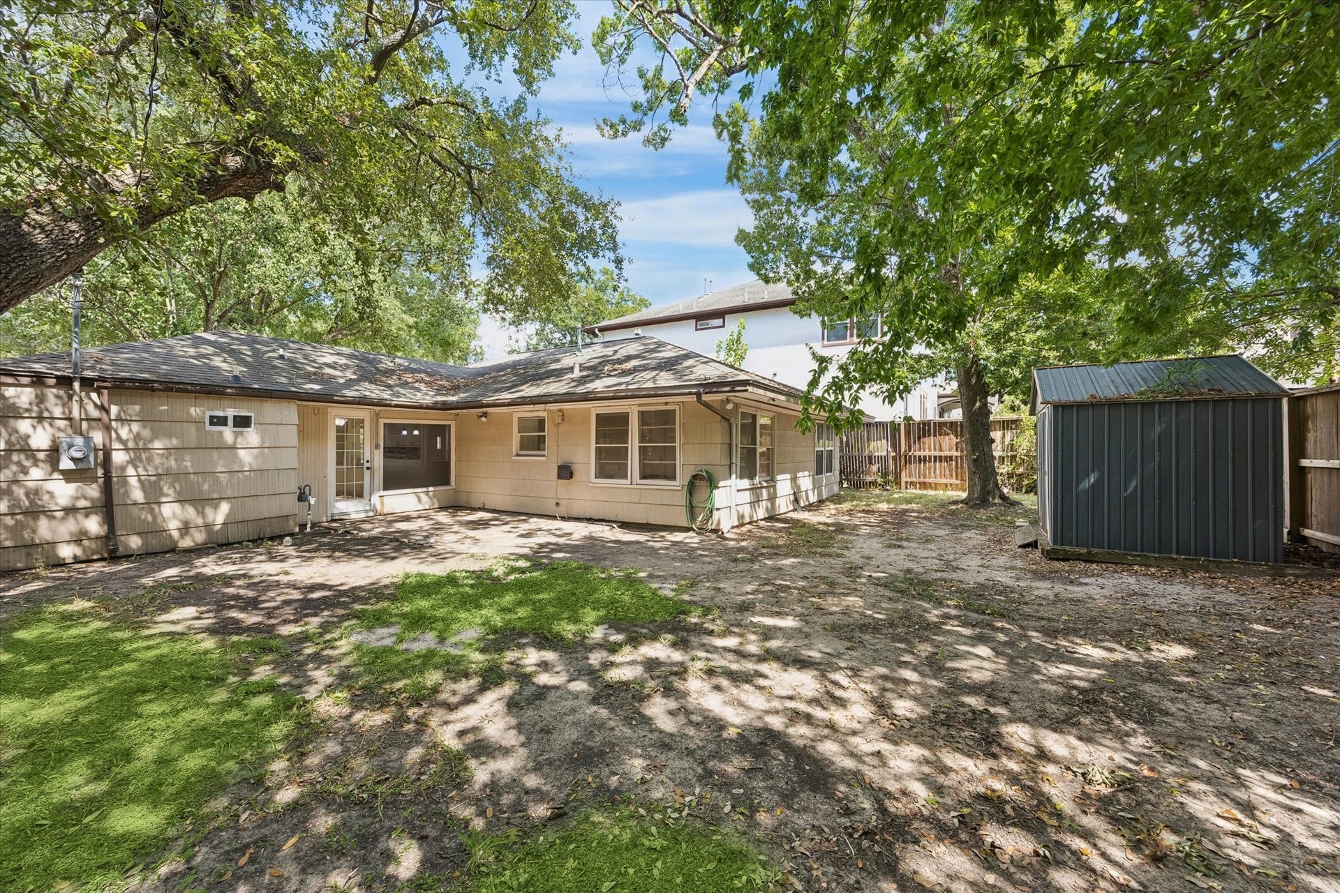 5119 PATRICK HENRY, Bellaire, TX 77401 Charming, shady backyard with mature trees, a cozy patio area, and a convenient storage shed.