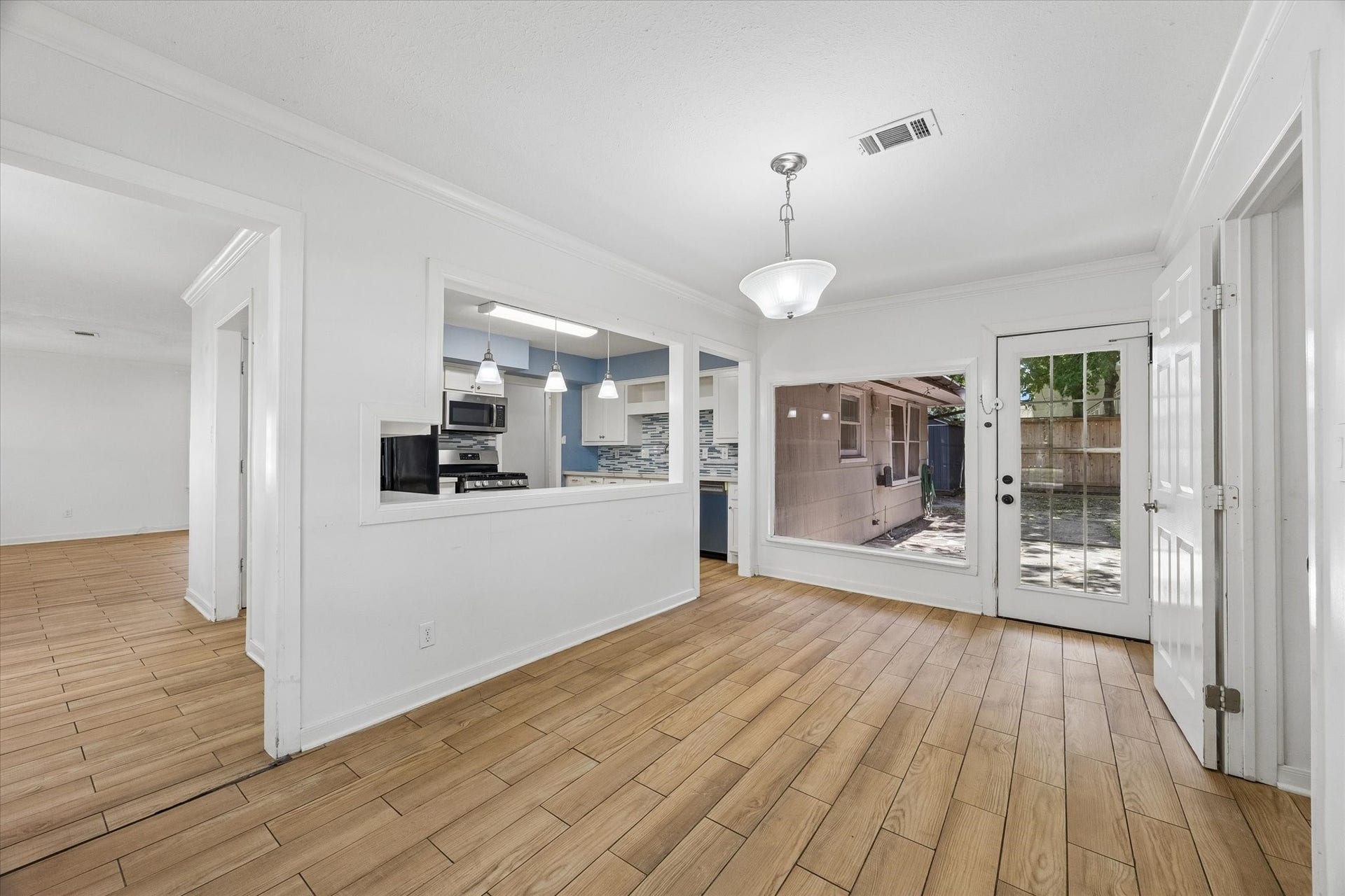 5119 PATRICK HENRY, Bellaire, TX 77401 A bright and inviting space featuring an open layout with wood-style tile flooring, a modern kitchen, and large windows offering abundant natural light and views of the backyard.