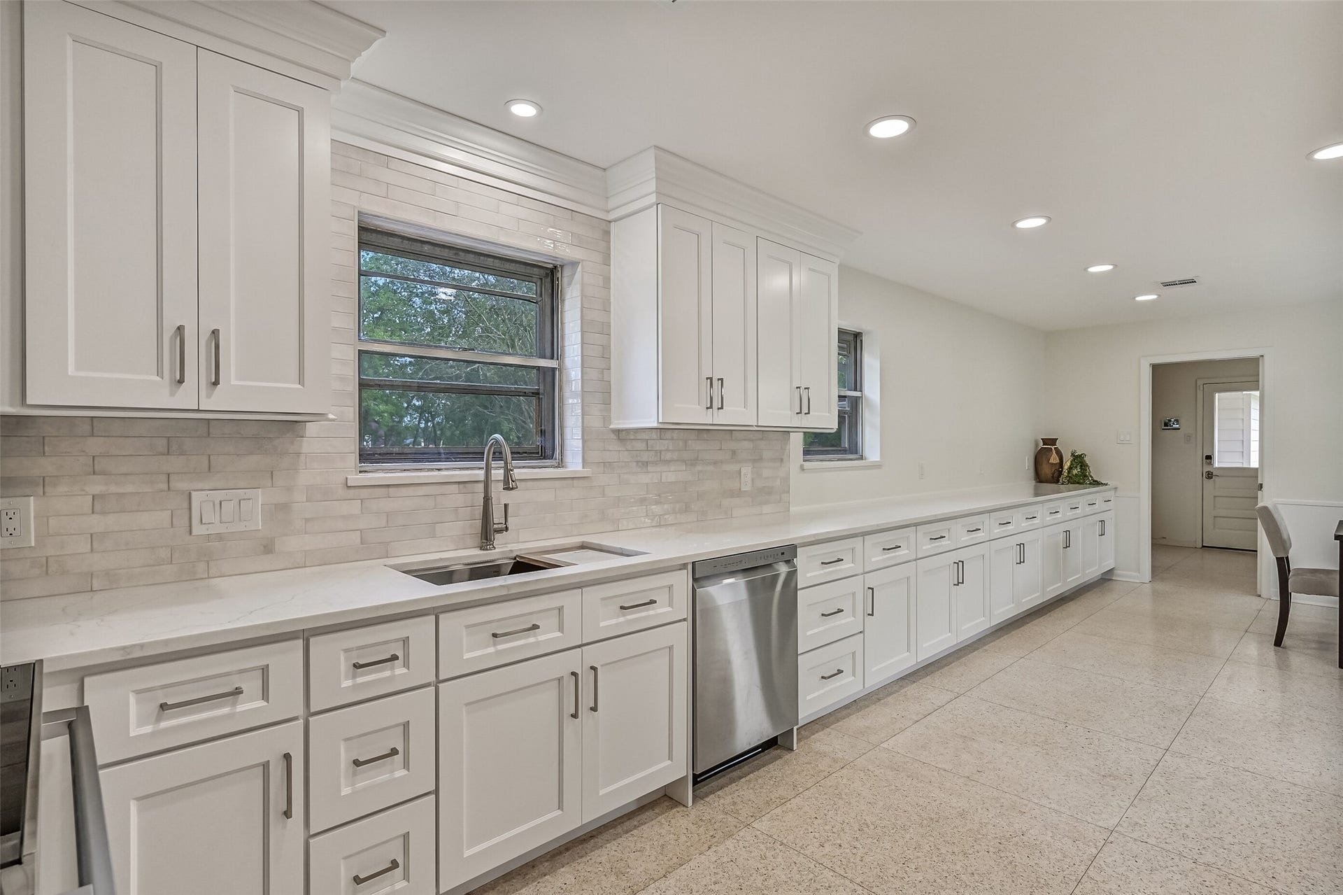 304 Chester Drive, Friendswood, TX 77546 Kitchen First Residence:
This view of the kitchen workspace highlights expansive quartz countertops, a dual basin sink positioned below a sunlit window, the new stainless dishwasher, complemented by abundant cabinetry and generous prep and serving surfaces extending into the breakfast room.