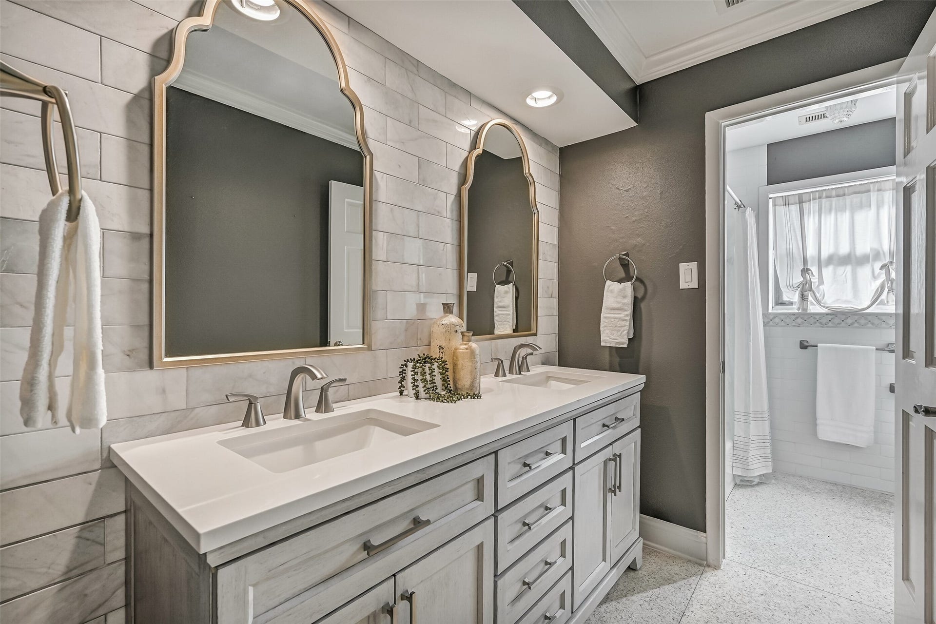 304 Chester Drive, Friendswood, TX 77546 Guest Bathroom First Residence:
The stylishly updated guest bath showcases a furniture-style double vanity with quartz countertops, dual undermount sinks, and custom framed mirrors set against a tiled accent wall. The bath includes a tub/shower combination with a classic white subway tile surround & decorative mosaic inlay.