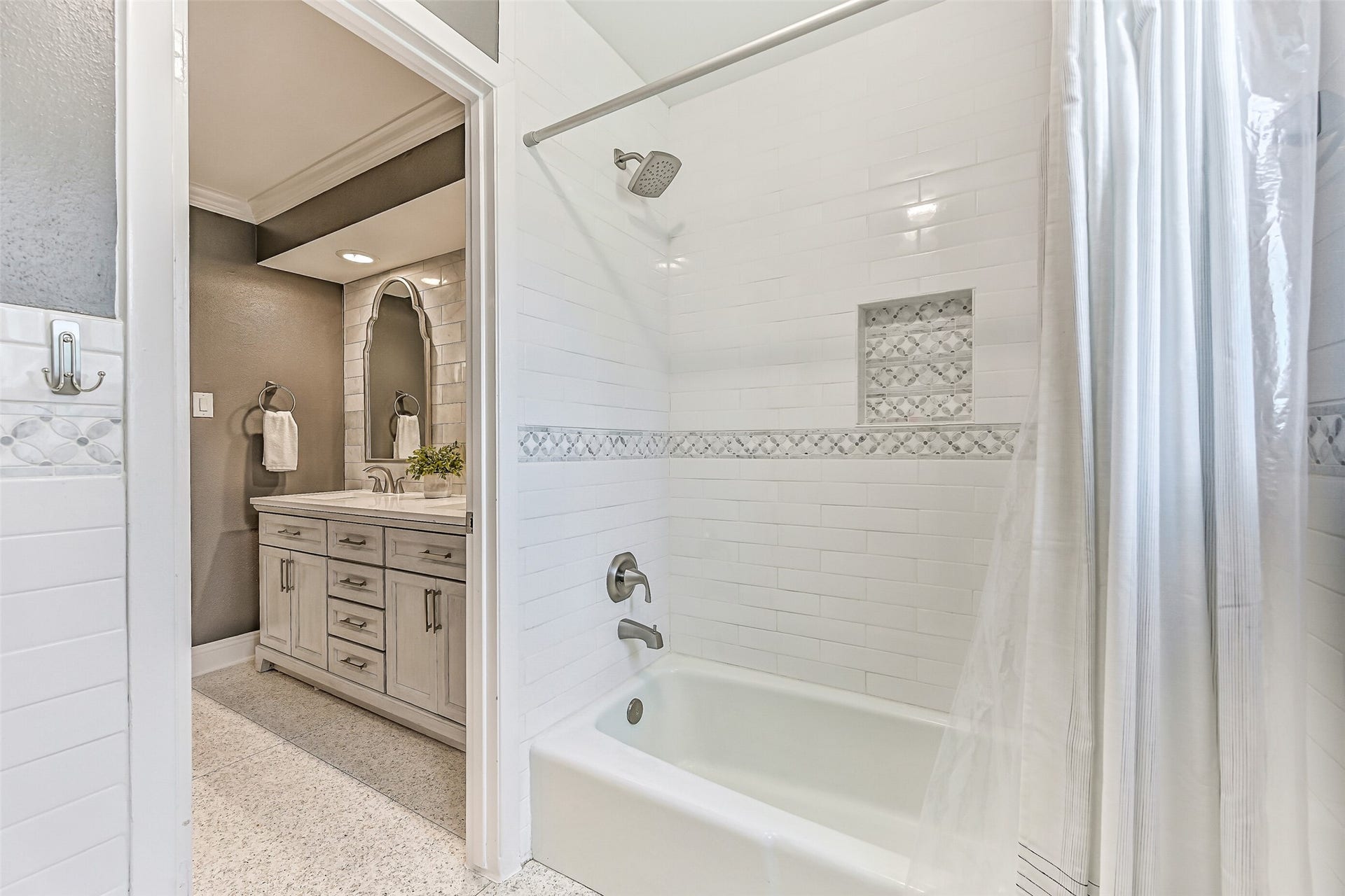 304 Chester Drive, Friendswood, TX 77546 Guest Bathroom First Residence:
The stylishly updated guest bath showcases a furniture-style double vanity with quartz countertops, dual undermount sinks, and custom framed mirrors set against a tiled accent wall. The bath includes a tub/shower combination with a classic white subway tile surround & decorative mosaic inlay.