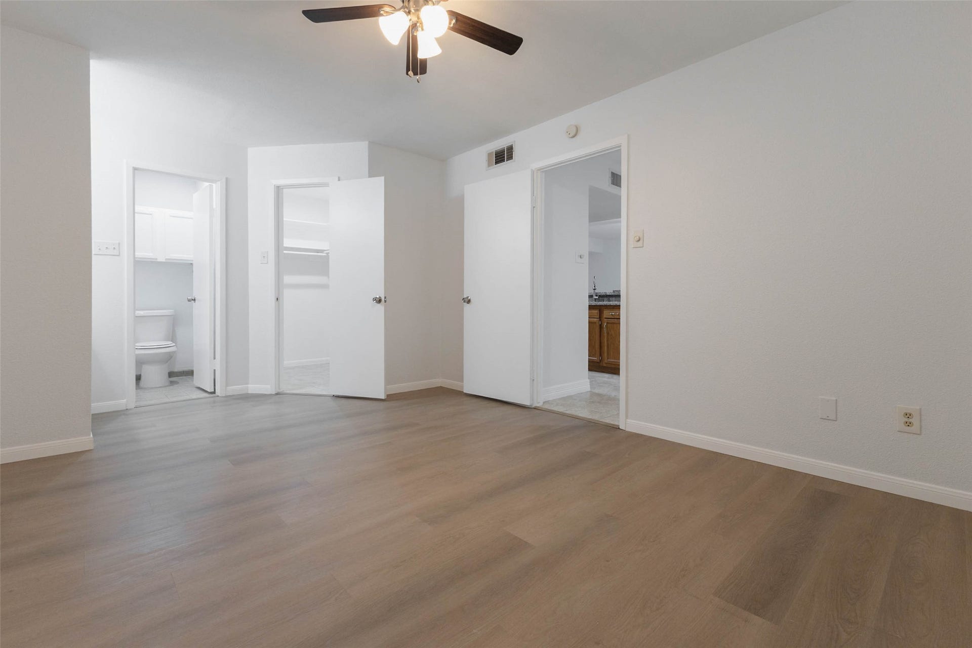 2800 Jeanetta Street, #2207, Houston, TX 77063 Spacious bedroom featuring sleek hardwood flooring, a ceiling fan, and convenient access to an ensuite bathroom and additional rooms.