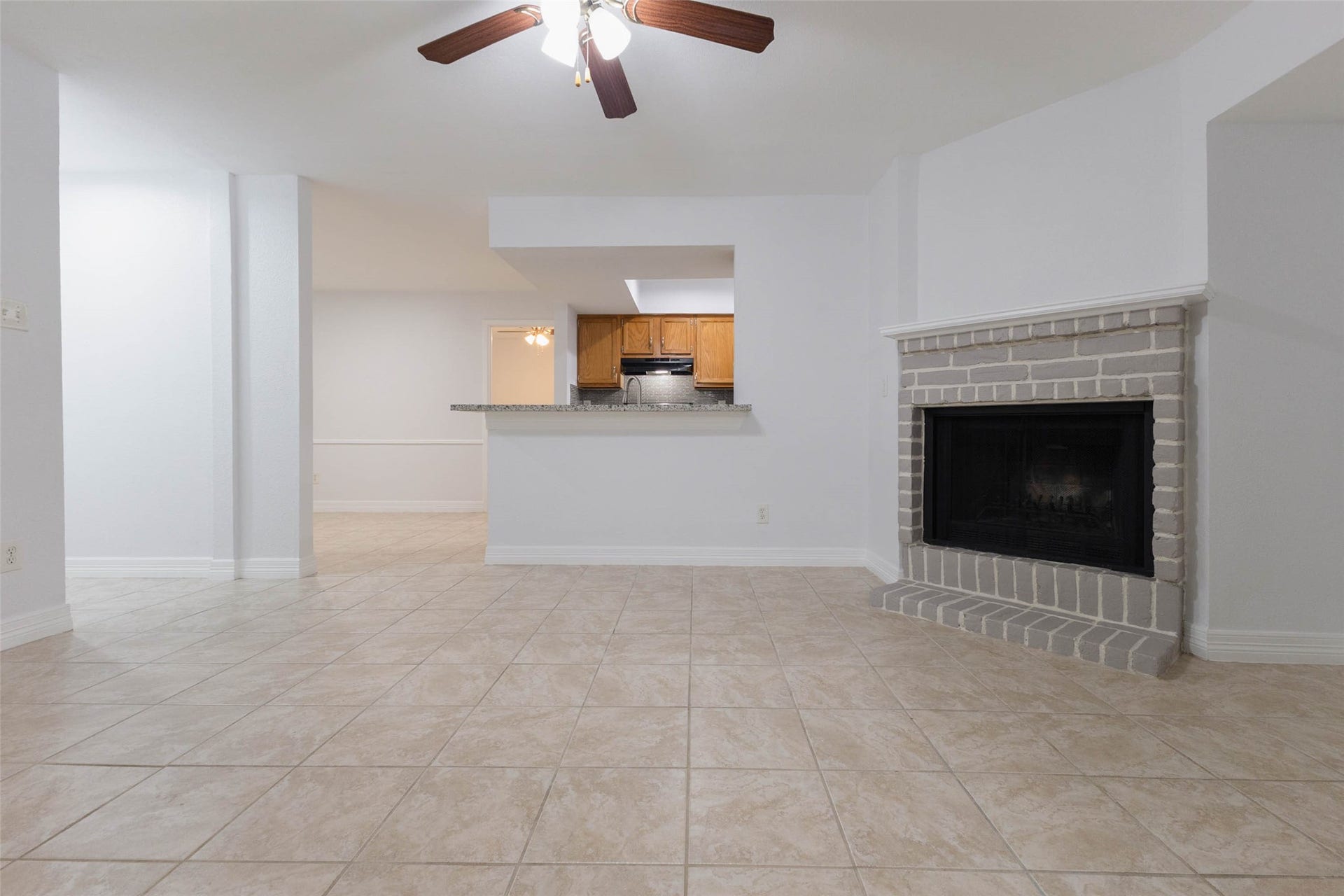 2800 Jeanetta Street, #2207, Houston, TX 77063 Spacious living area with elegant tile flooring, a cozy brick fireplace, and an open layout leading to a modern kitchen with granite countertops and wooden cabinetry.