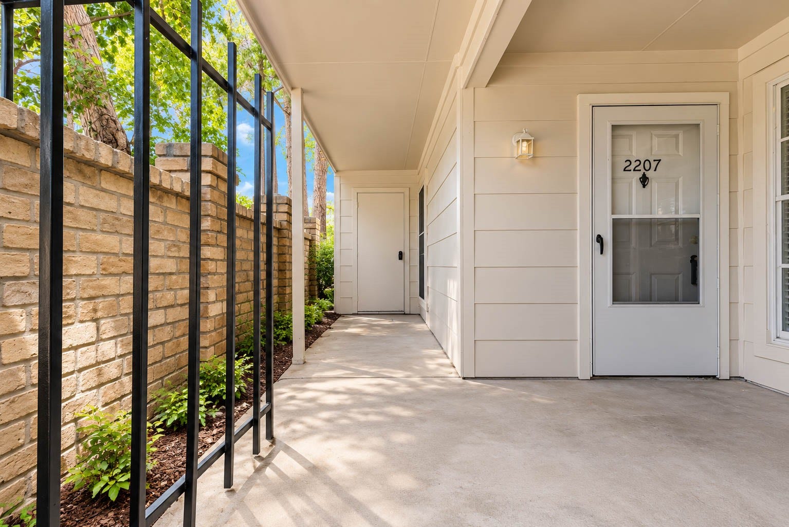 2800 Jeanetta Street, #2207, Houston, TX 77063 Charming front entry with a covered walkway, accented by a brick wall and lush greenery, leading to a welcoming door.