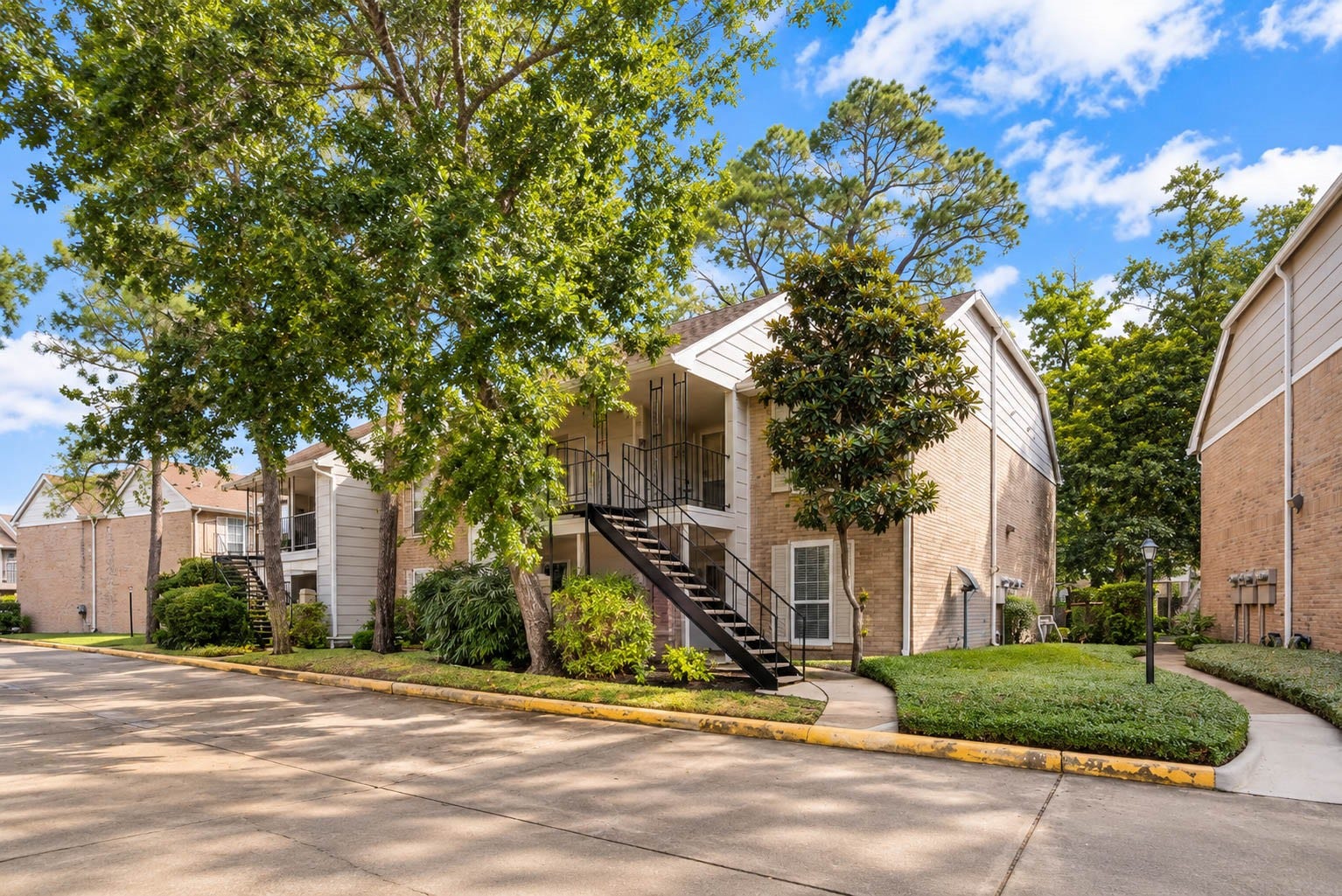 2800 Jeanetta Street, #2207, Houston, TX 77063 Charming two-story brick apartment surrounded by lush greenery, featuring a welcoming staircase entrance and situated in a peaceful neighborhood.