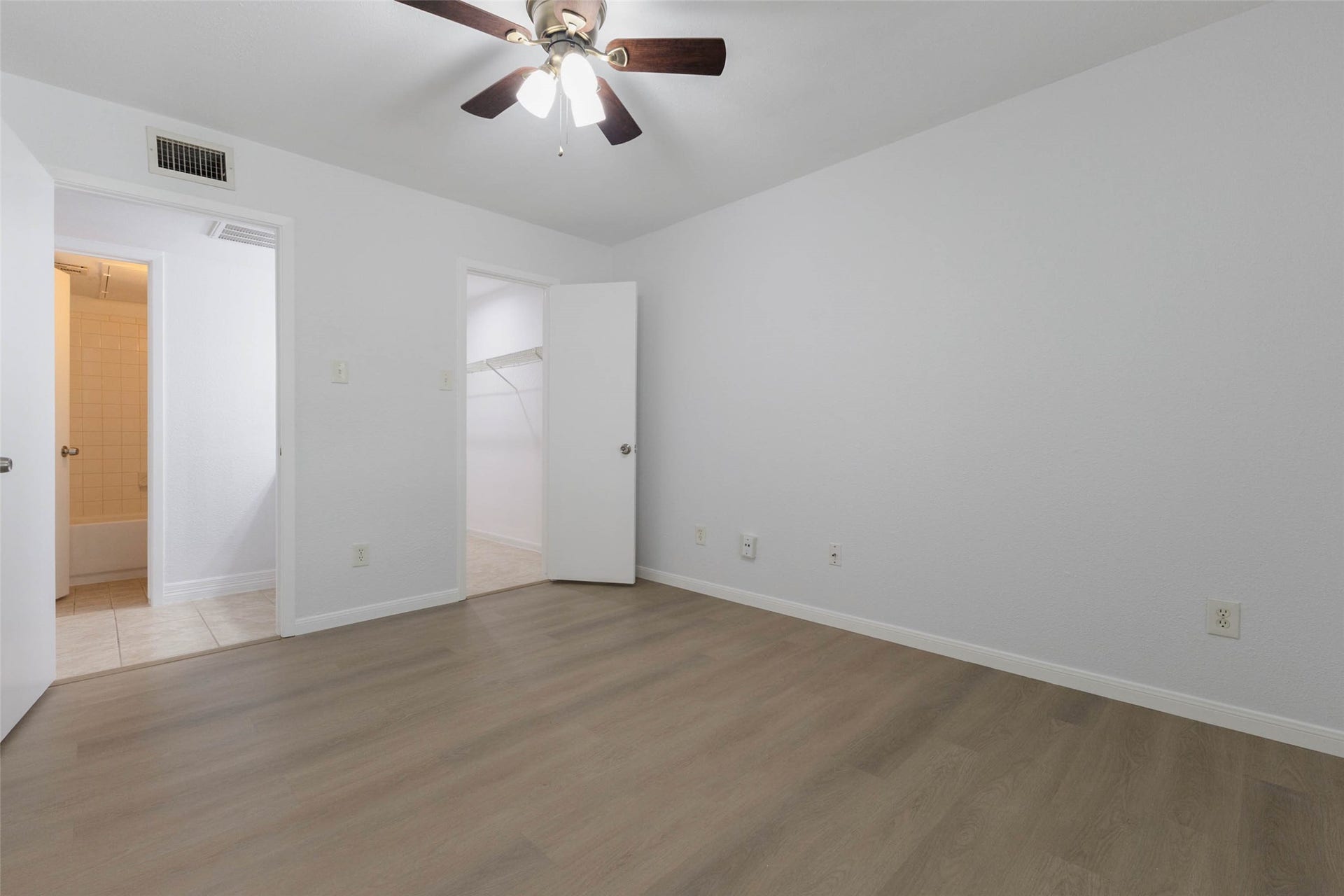 2800 Jeanetta Street, #2207, Houston, TX 77063 Bright bedroom with sleek wood flooring, ceiling fan, and convenient access to a walk-in closet and en-suite bathroom.