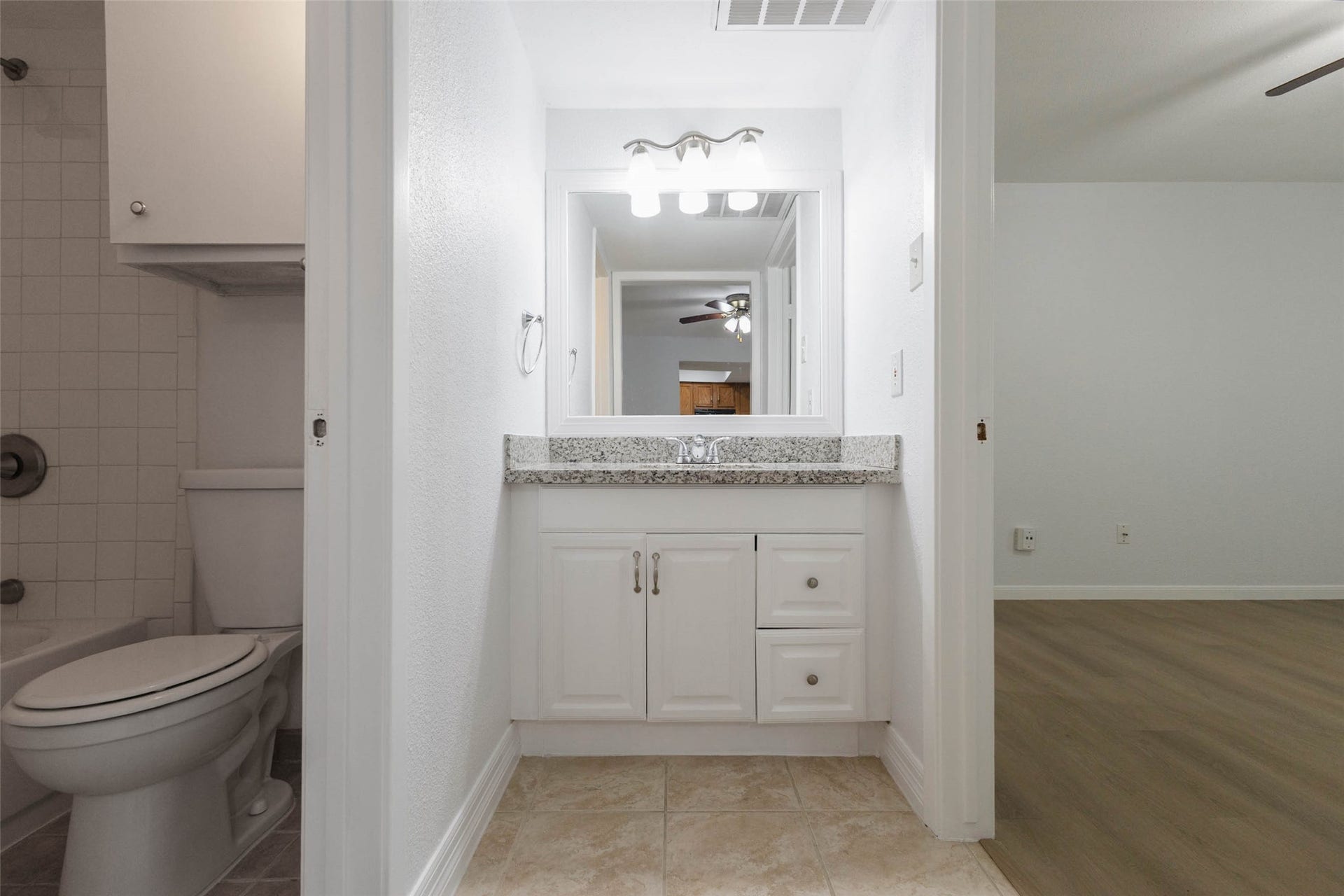 2800 Jeanetta Street, #2207, Houston, TX 77063 Bright bathroom with a granite countertop, modern fixtures, and adjacent tiled shower, flowing into a spacious room with sleek wood flooring.