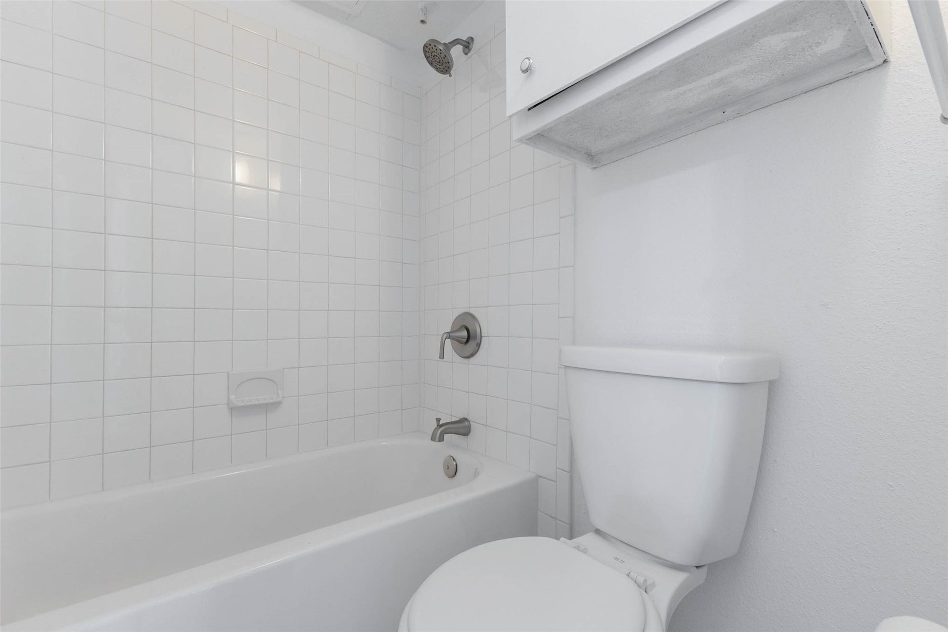 2800 Jeanetta Street, #2207, Houston, TX 77063 Bright and clean bathroom featuring a classic white tiled shower-tub combo and convenient overhead storage.