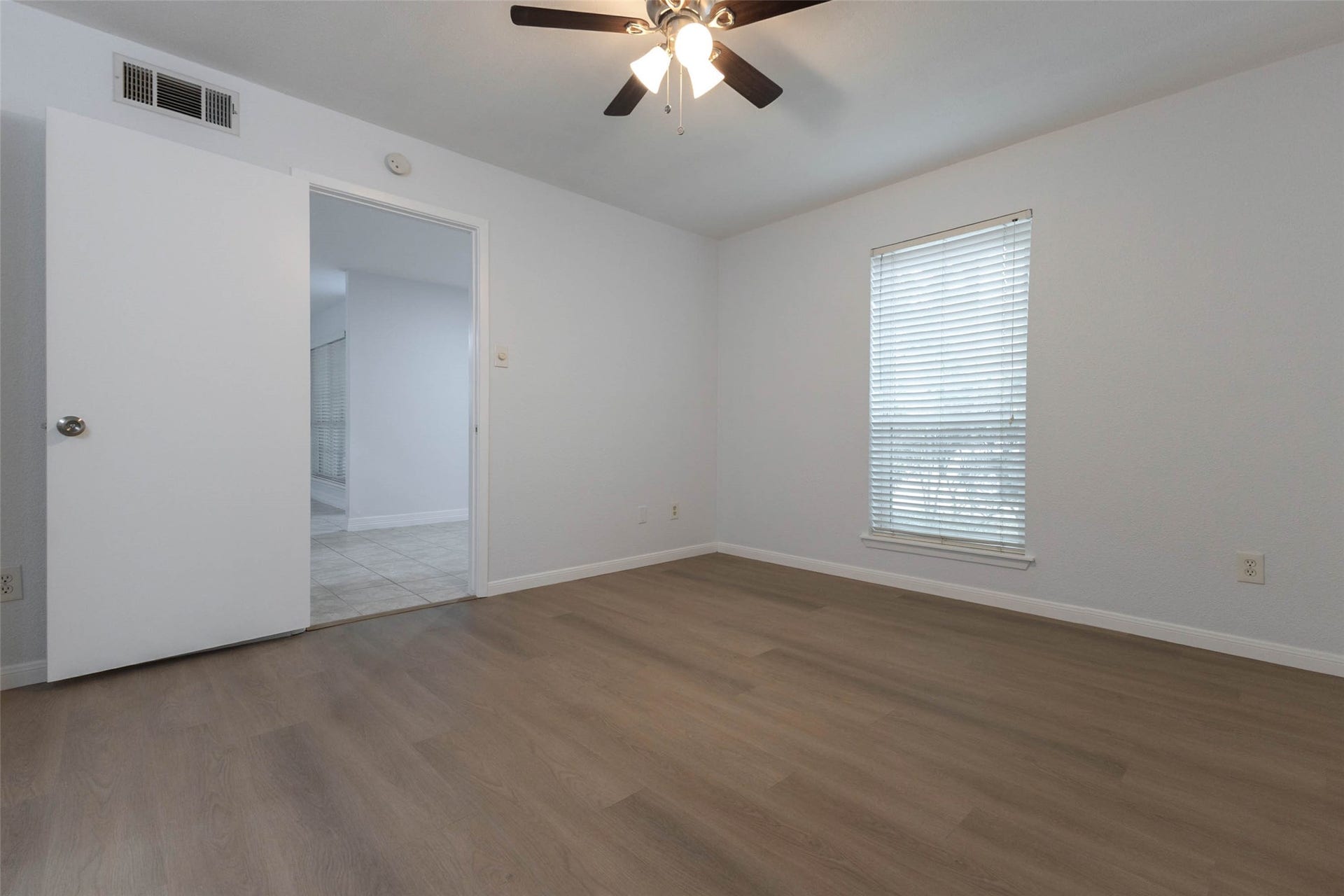 2800 Jeanetta Street, #2207, Houston, TX 77063 Bright and inviting bedroom with sleek wood flooring, a ceiling fan, and ample natural light from a large window.