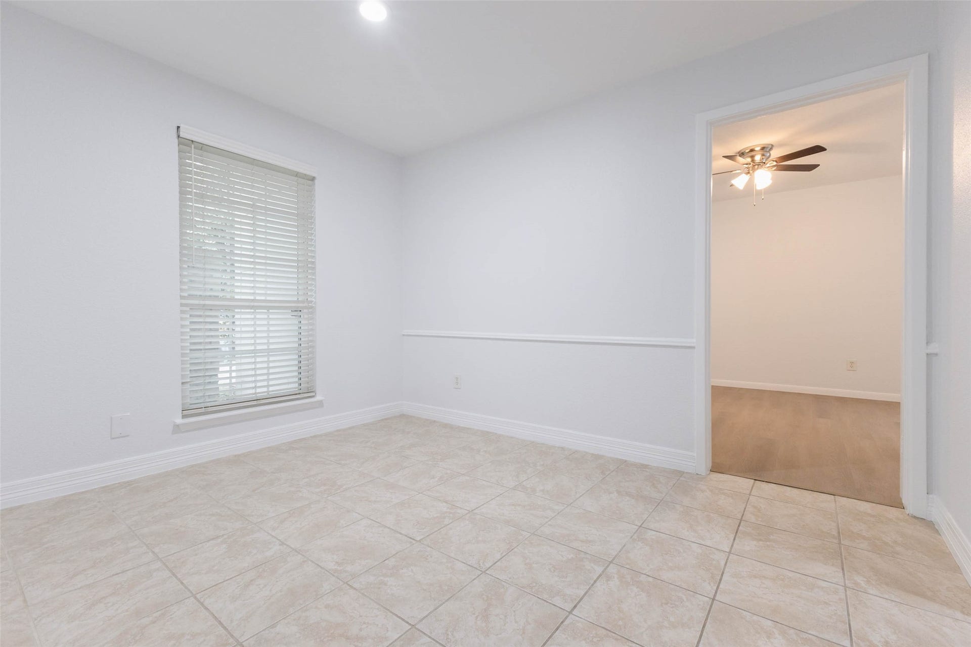 2800 Jeanetta Street, #2207, Houston, TX 77063 Bright and airy room featuring tile flooring and a large window with blinds, leading to an adjacent space with a ceiling fan and wood flooring.