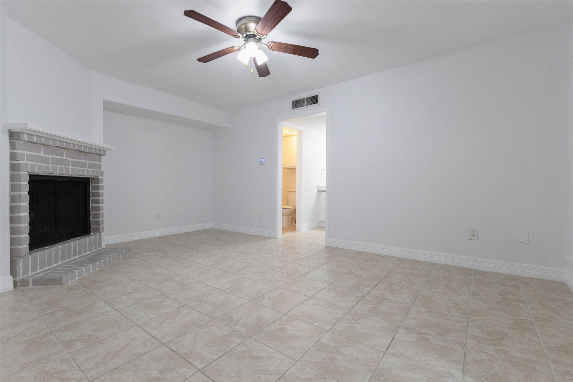 2800 Jeanetta Street, #2207, Houston, TX 77063 Spacious living area with a cozy brick fireplace, ceiling fan, and tile flooring, leading to a bathroom for convenience.