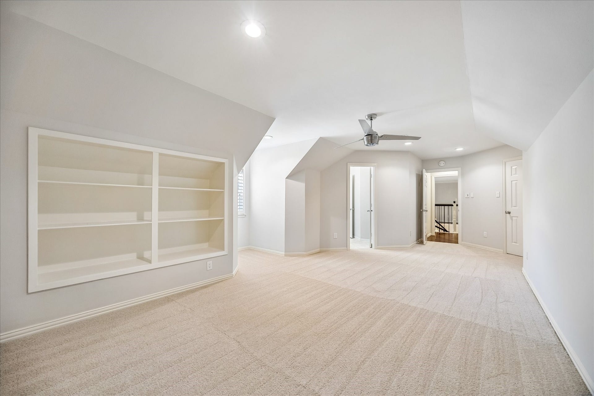 This spacious secondary bedroom features built-in shelving, recessed lighting, and a ceiling fan, highlighted by a striking angled ceiling with a charming alcove. The architectural detail adds character and dimension, creating a warm and inviting retreat with a refined, custom feel.