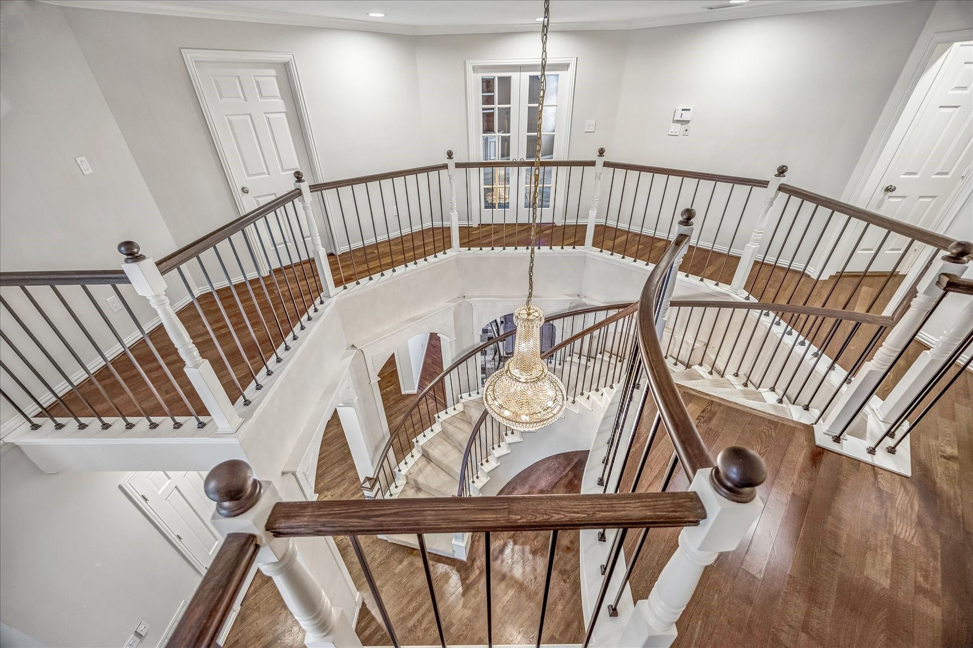 This photo showcases a stunning circular staircase and a grand chandelier as its focal point. The surrounding spacious, well-lit landing features multiple elegant doorways, enhancing the homes sense of scale, sophistication, and architectural grandeur.