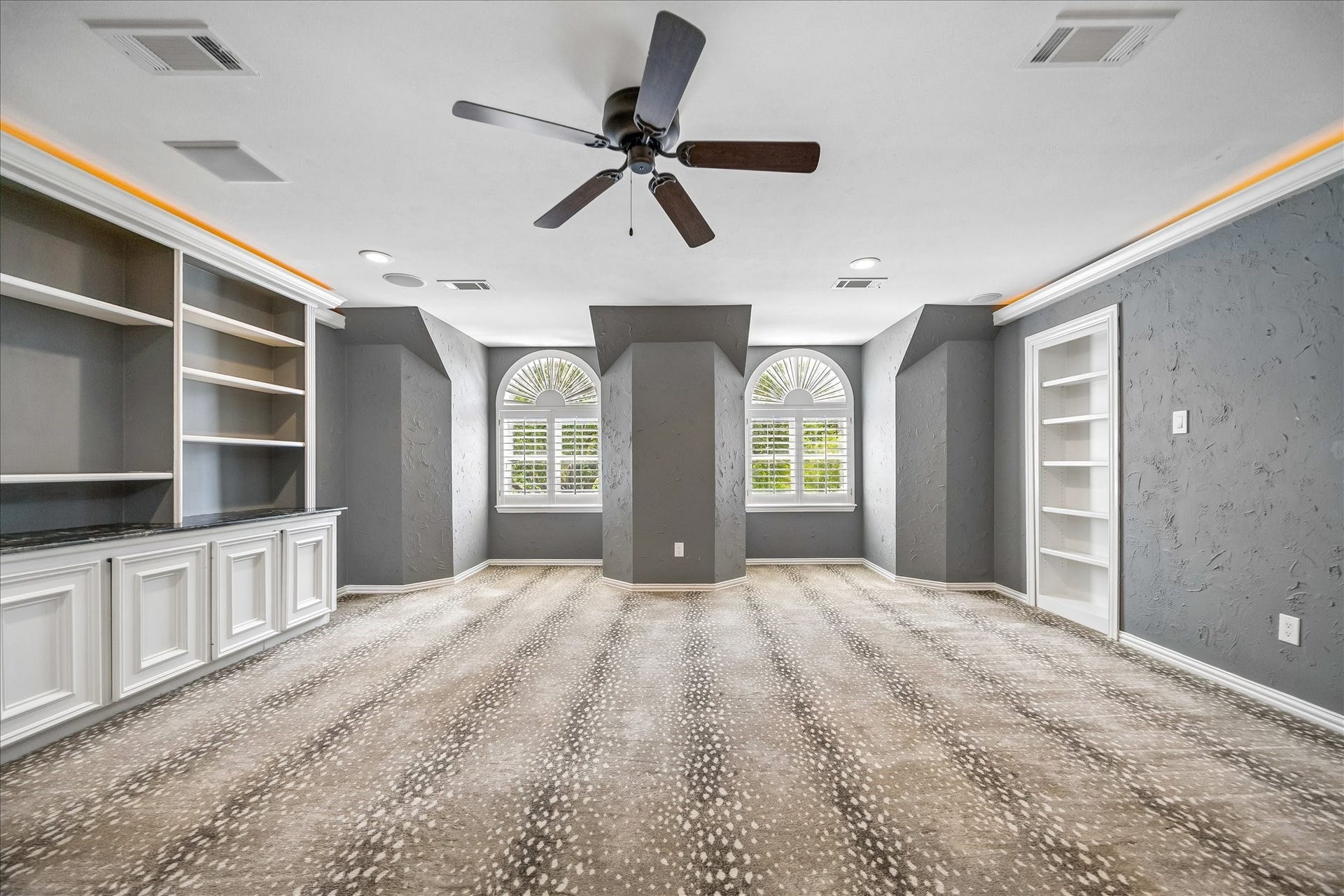 Fun times! The upstairs game room features built-in shelving and cabinetry, a ceiling fan, and  arched windows with shutters that fill the space with natural light.