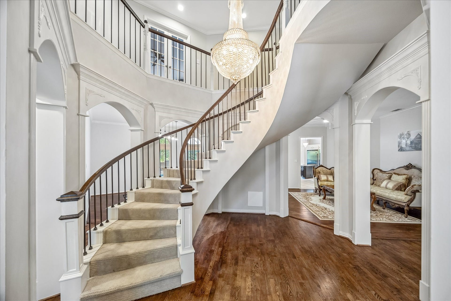 An elegant entryway featuring a grand curved staircase, a stunning chandelier, and hardwood floors. Arched doorways lead to additional rooms, adding to the sophisticated ambiance.