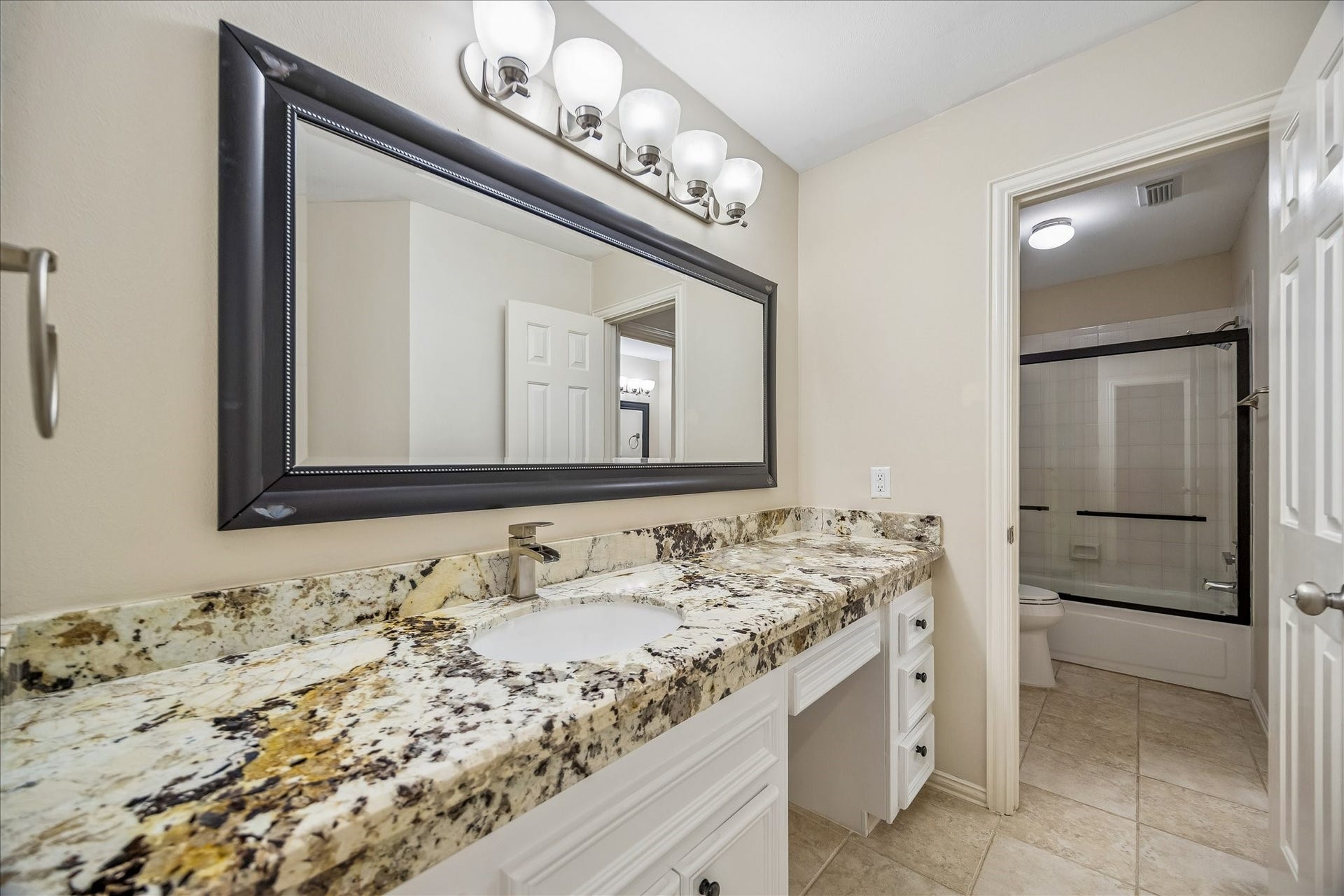 One of two beautifully updated, upstairs bathrooms. This space showcases a granite countertop, and a large framed mirror. A bathtub, with glass enclosure and elegant tile flooring, complete the space.