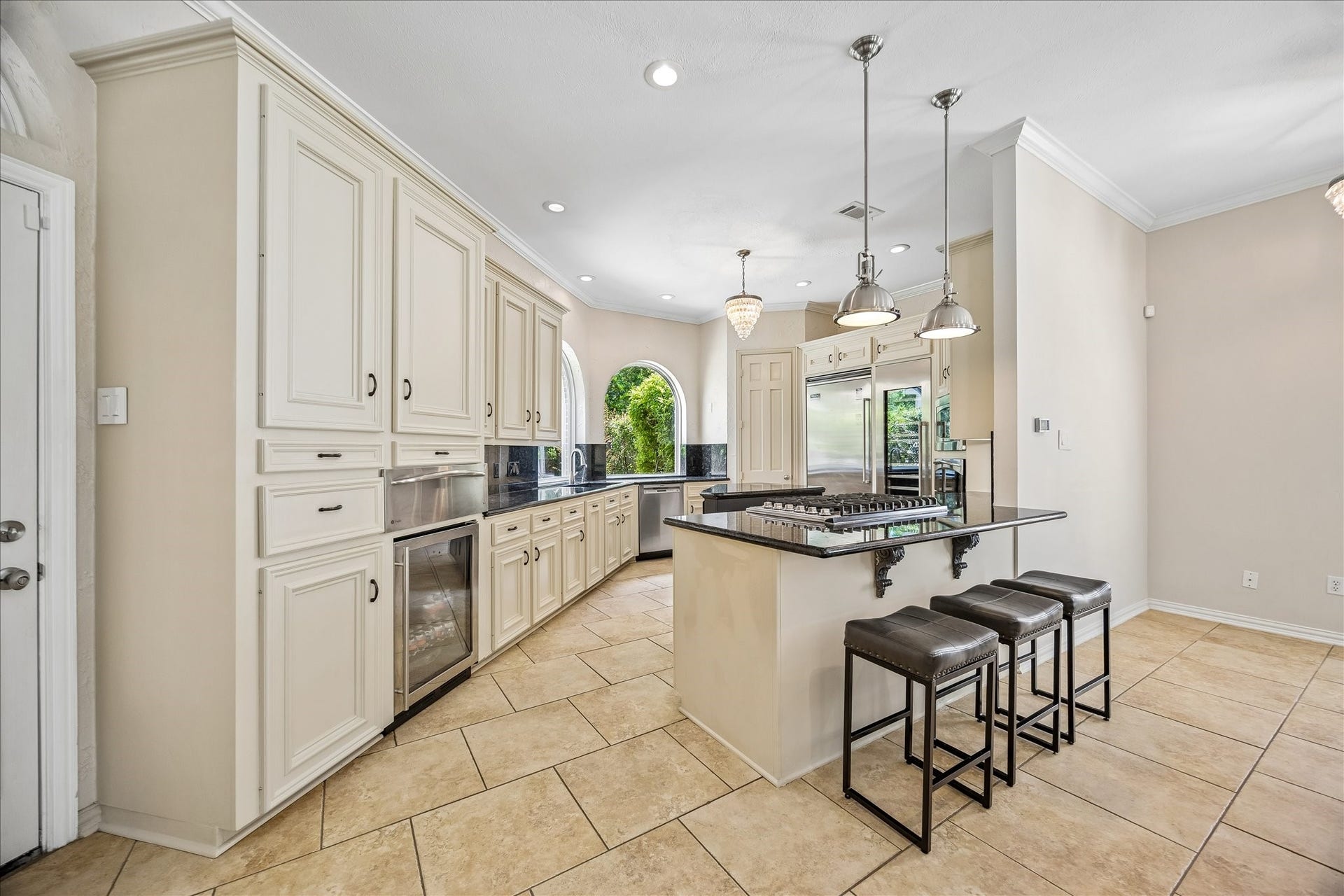 Designed with both function and style in mind, the chef's dream kitchen features a beverage refrigerator, a five-burner gas cooktop, and elegant pendant lighting. Abundant natural light streams through the arched windows, creating a bright and inviting atmosphere. Open to the den, the kitchen offers a layout that is perfect for entertaining and everyday living.